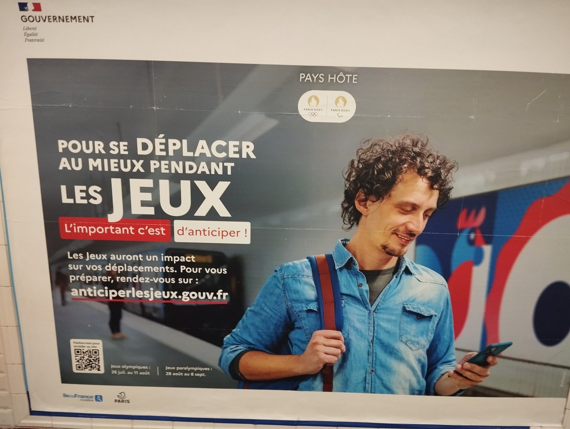 Publicité dans le métro pour les JO avec écrit "Pour se déplacer au mieux pendant les jeux, l'important c'est d'anticiper ! Les jeux auront un impact sur vos déplacements. Pour vous préparer, rendez vous sur : anticiper les jeux point gouv point fr"