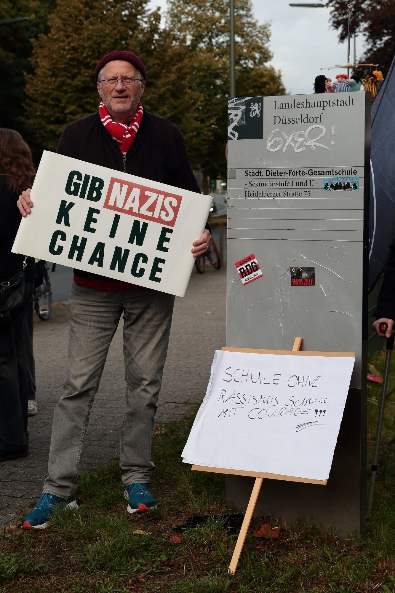 Der pensionierte Lehrer Kasper Michels mit einem Schild "Gib Nazis keine Chance" neben einem Schild "Schule ohne Rassismus.  Schule mit Courage".