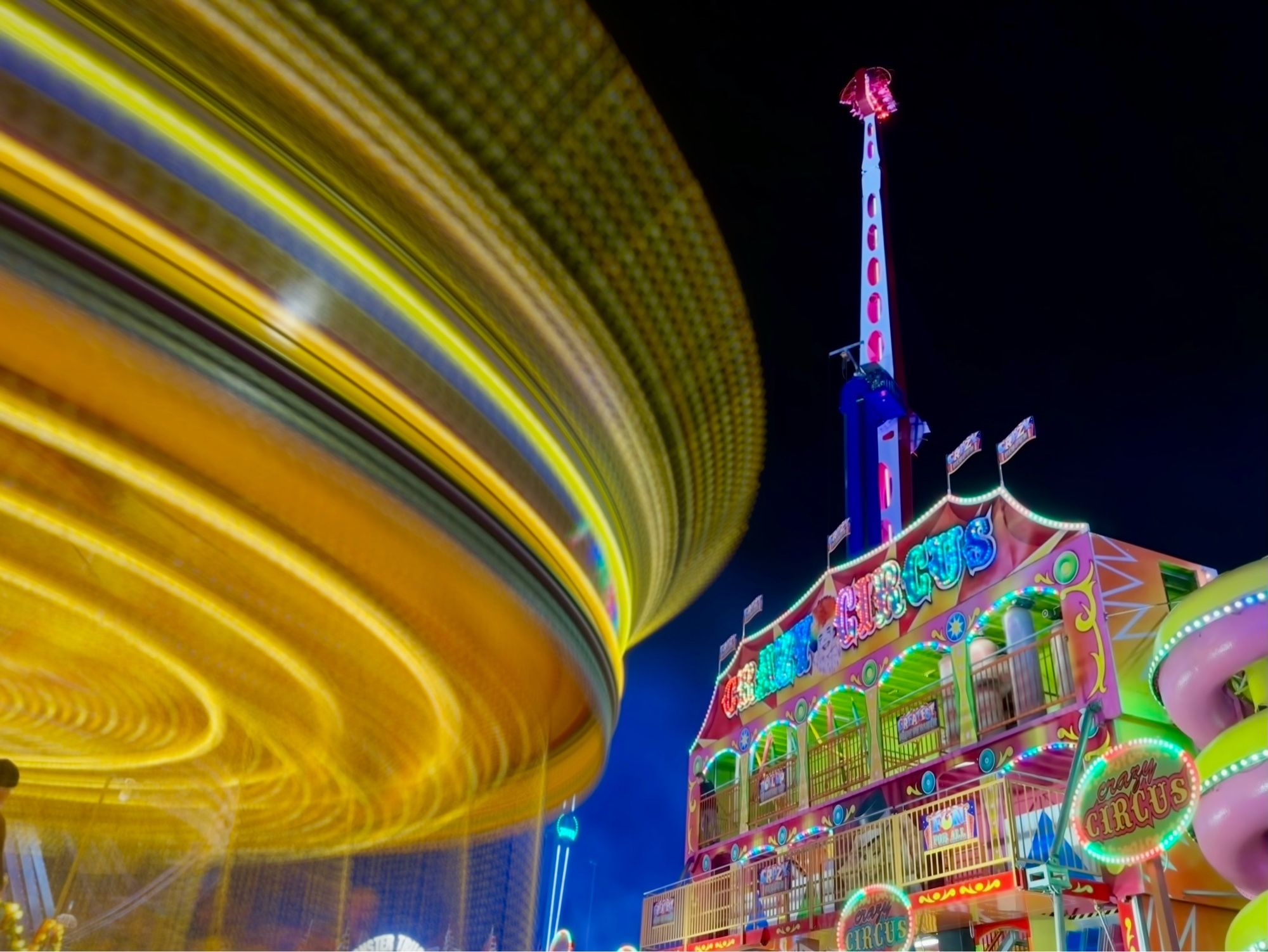 A long exposure image with a twirling carousel of lights on the left-hand side and an illuminated house of fun on the right