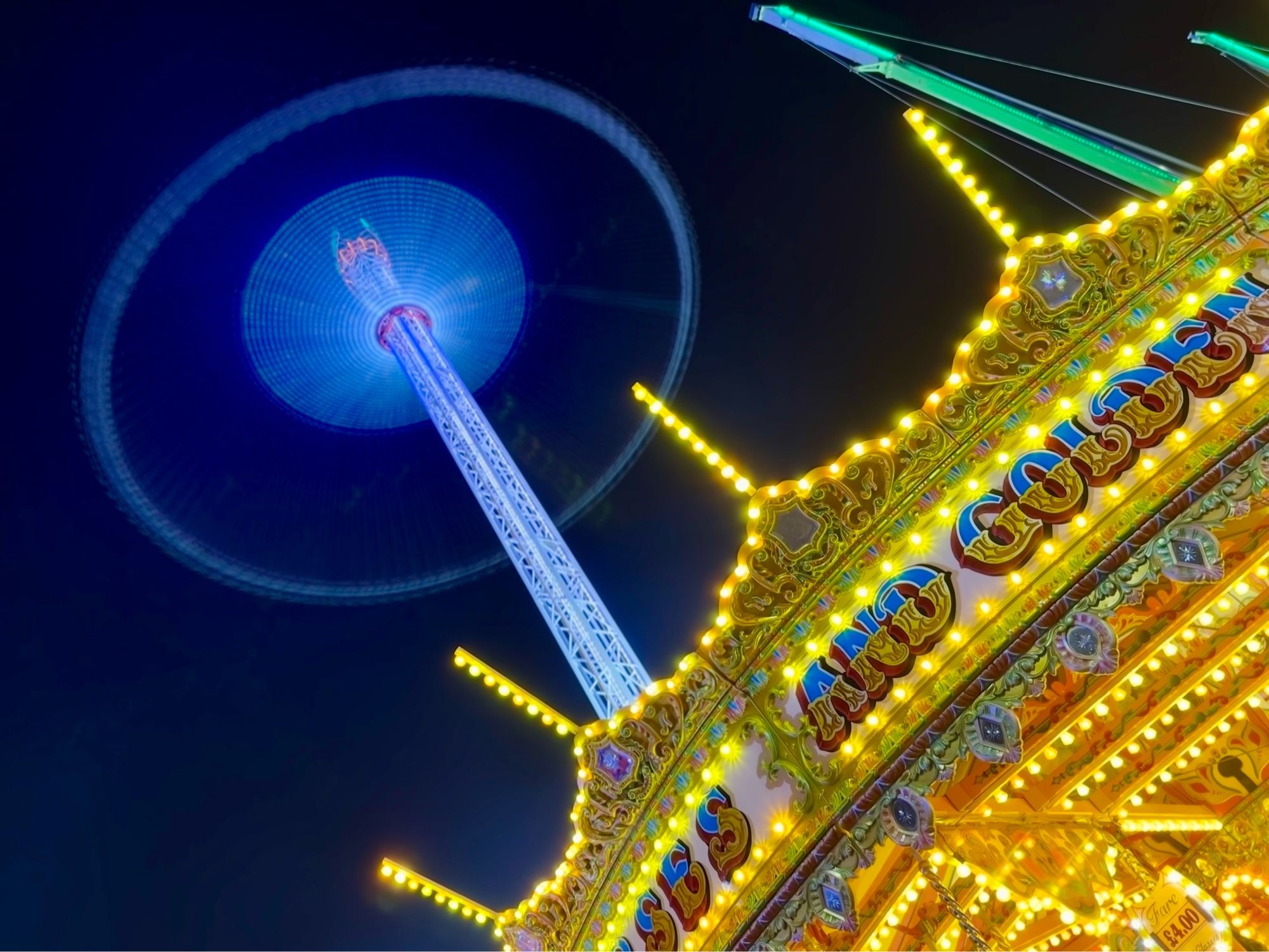 An illuminated carousel with a circle of light in the background caused by a long exposure and a fairground ride that twirls people around