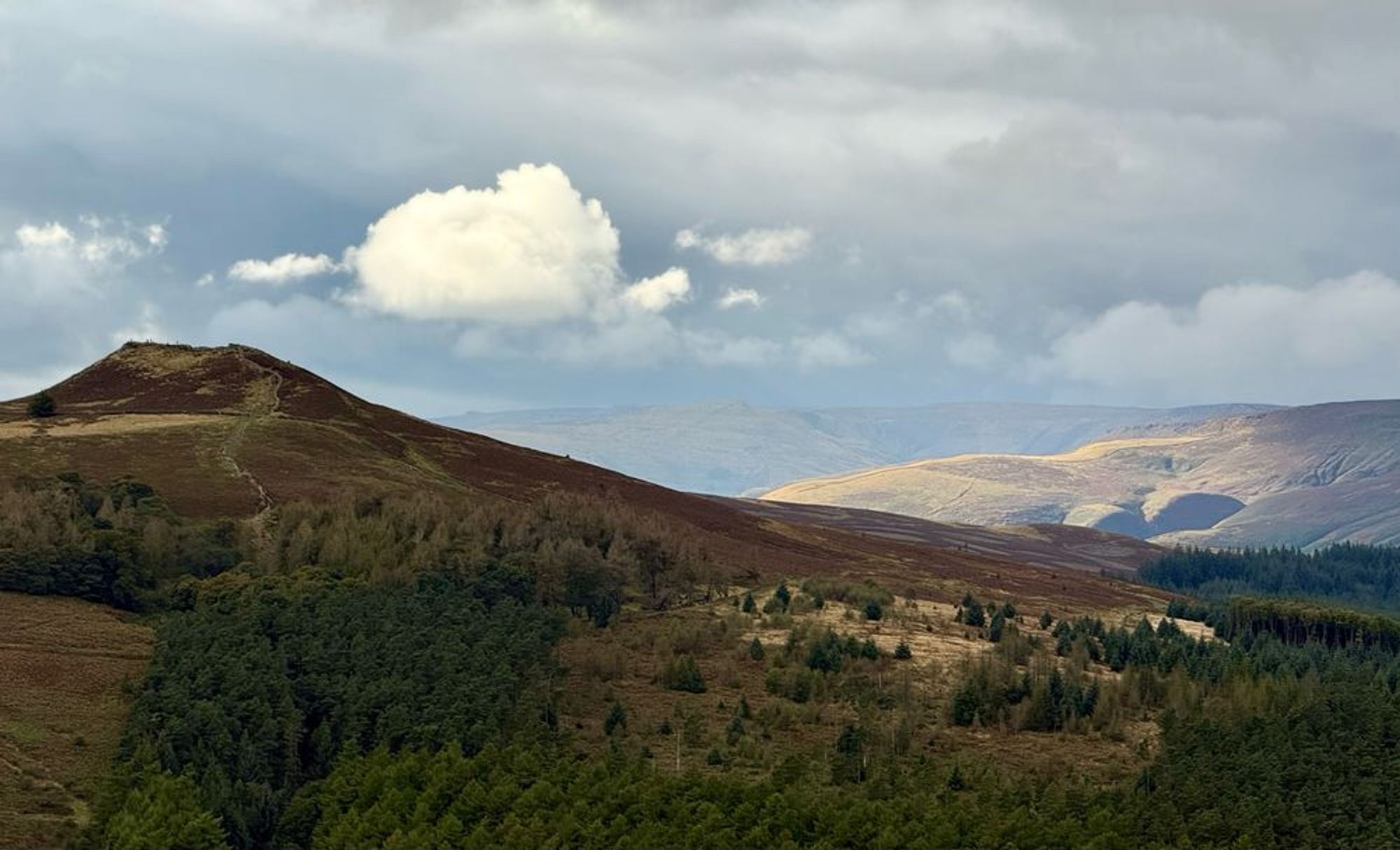 A single illuminated cloud about a peak, with dark clouds in the background and reddish bracken on the side of the hill in the foreground