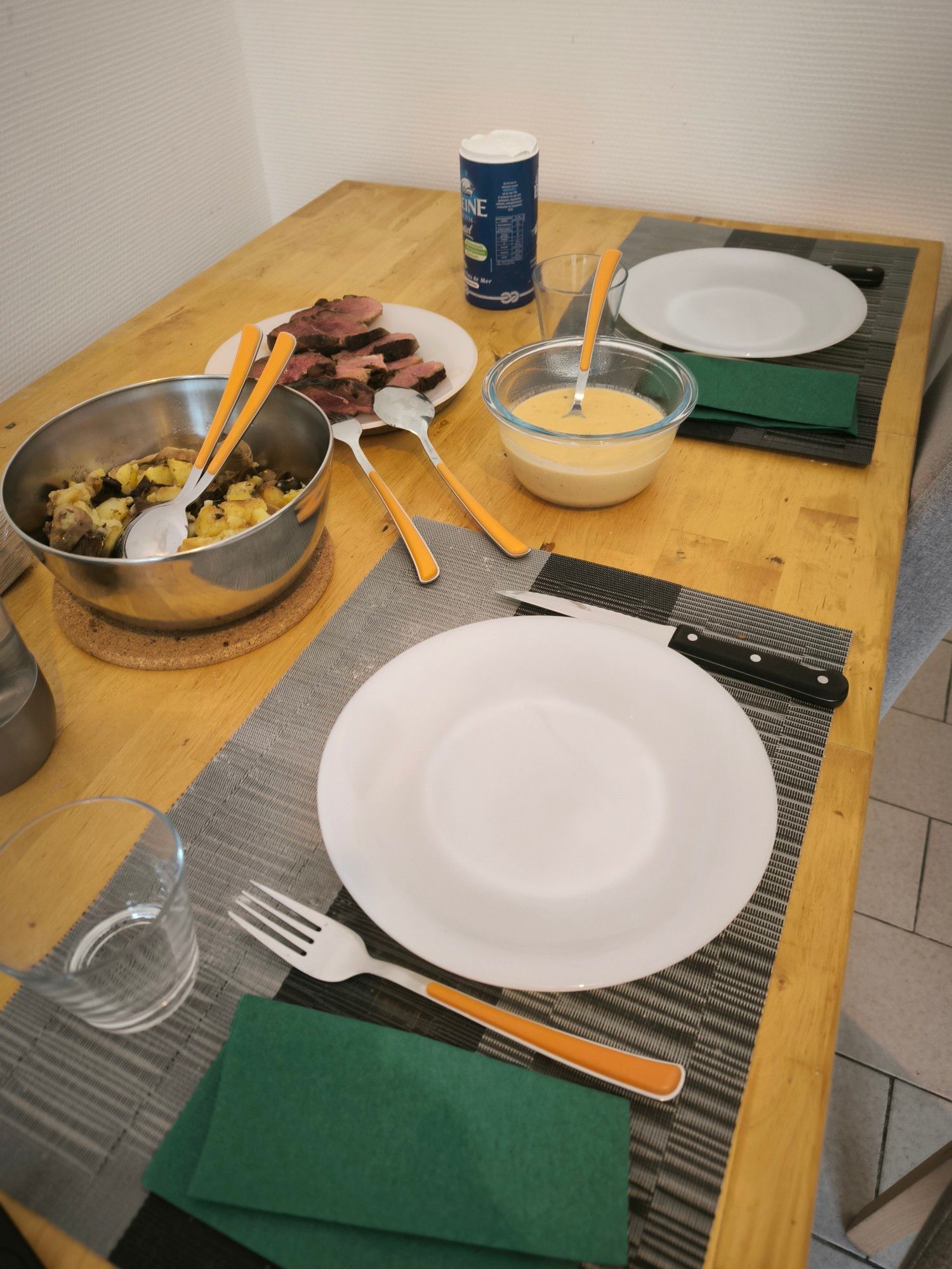 Table avec les plats séparés : patates et champignons forestiers, magret et sauce. 2 assiettes, couverts.