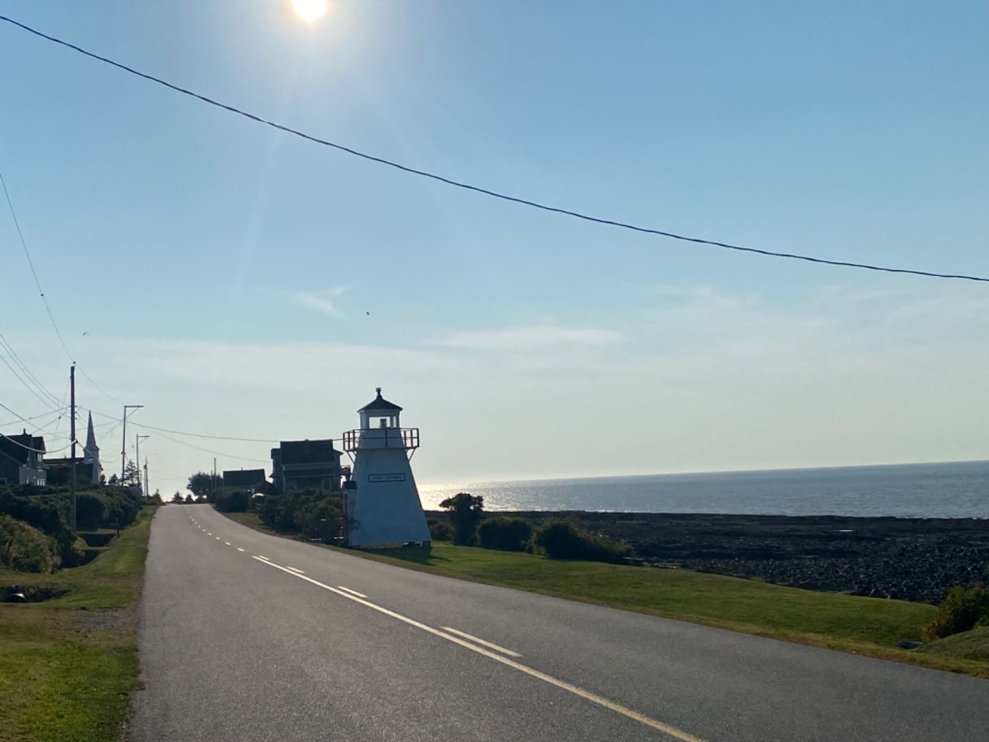 Nova Scotian lighthouse, road in foreground, bay in background. Sun starting to set. 