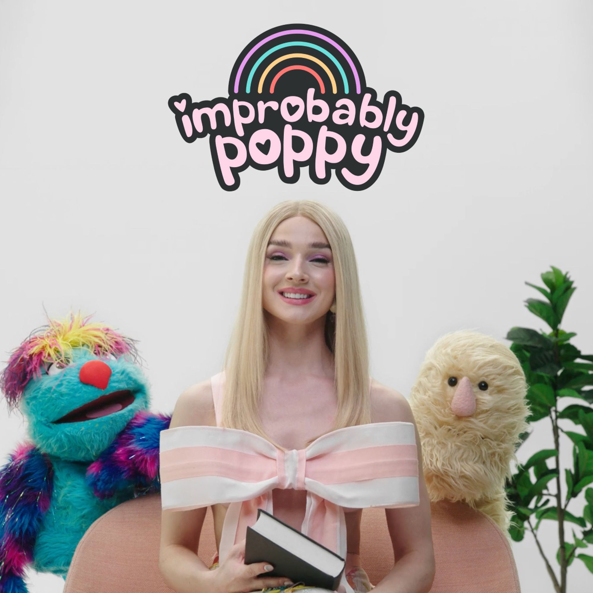 Capa da série "Improbably Poppy" onde Poppy está olhando para a câmera sorrindo e segurando um livro enquanto dois bichos apeluciados e uma planta estão atrás dela. Ela está sentada numa poltrona rosada.