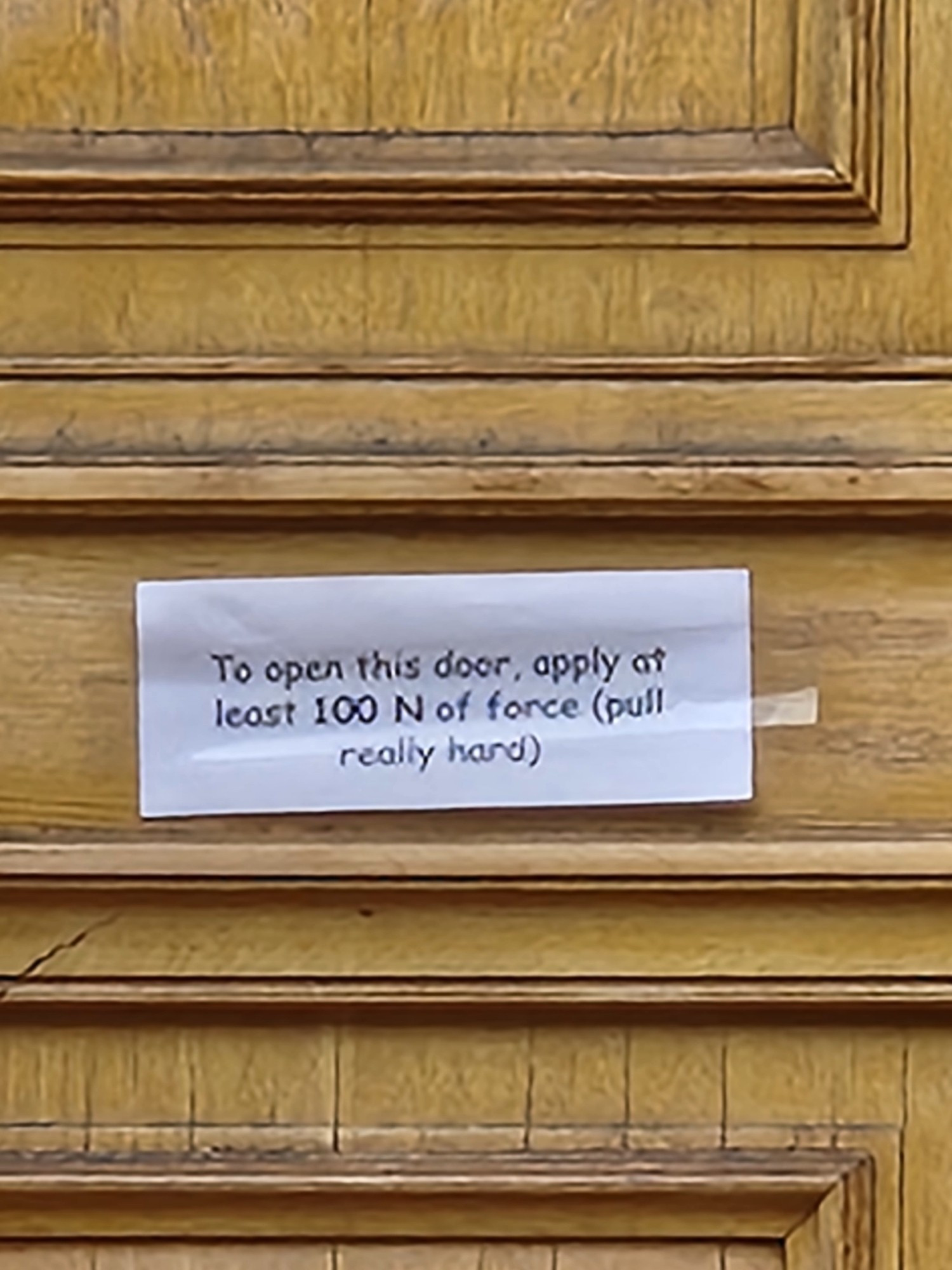 A note on the door of the physics building that reads, "to open this door, apply at least 100 N of force (pull really hard)"