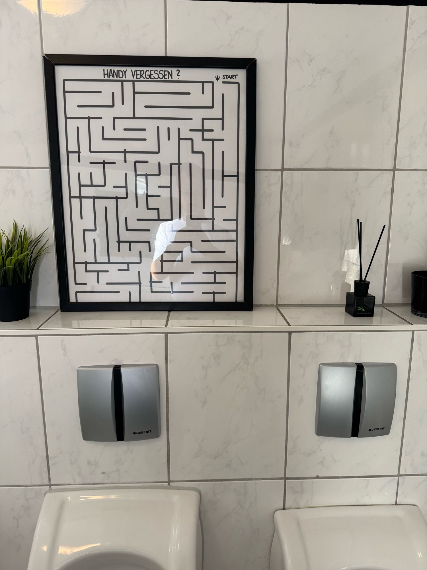 Labyrinth-Bild über einem Pissoir, darin steht: Handy vergessen?