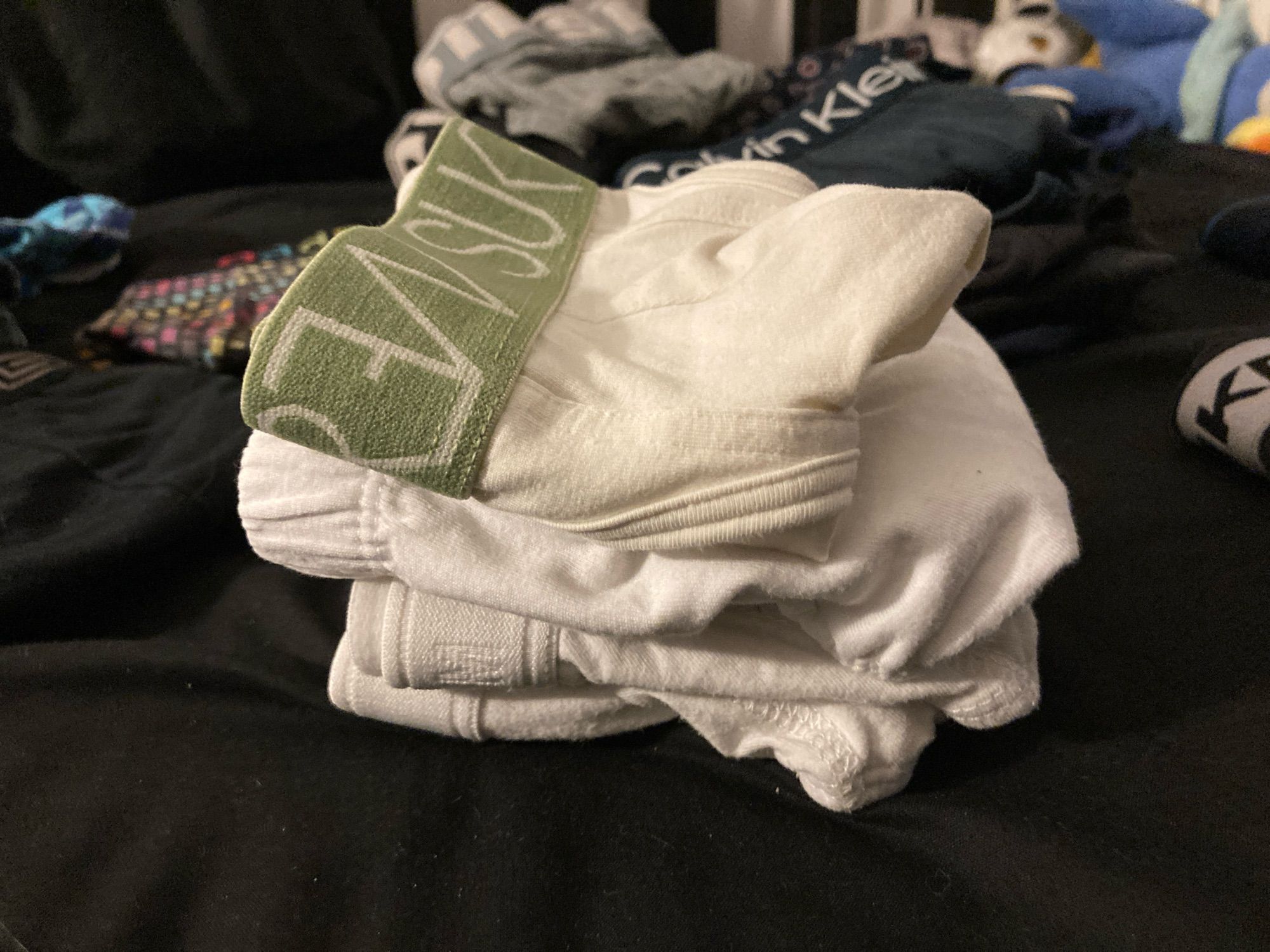 four pairs of folded briefs stacked on each other, all of which are white. the top one has a green waistband, the rest are entirely white.