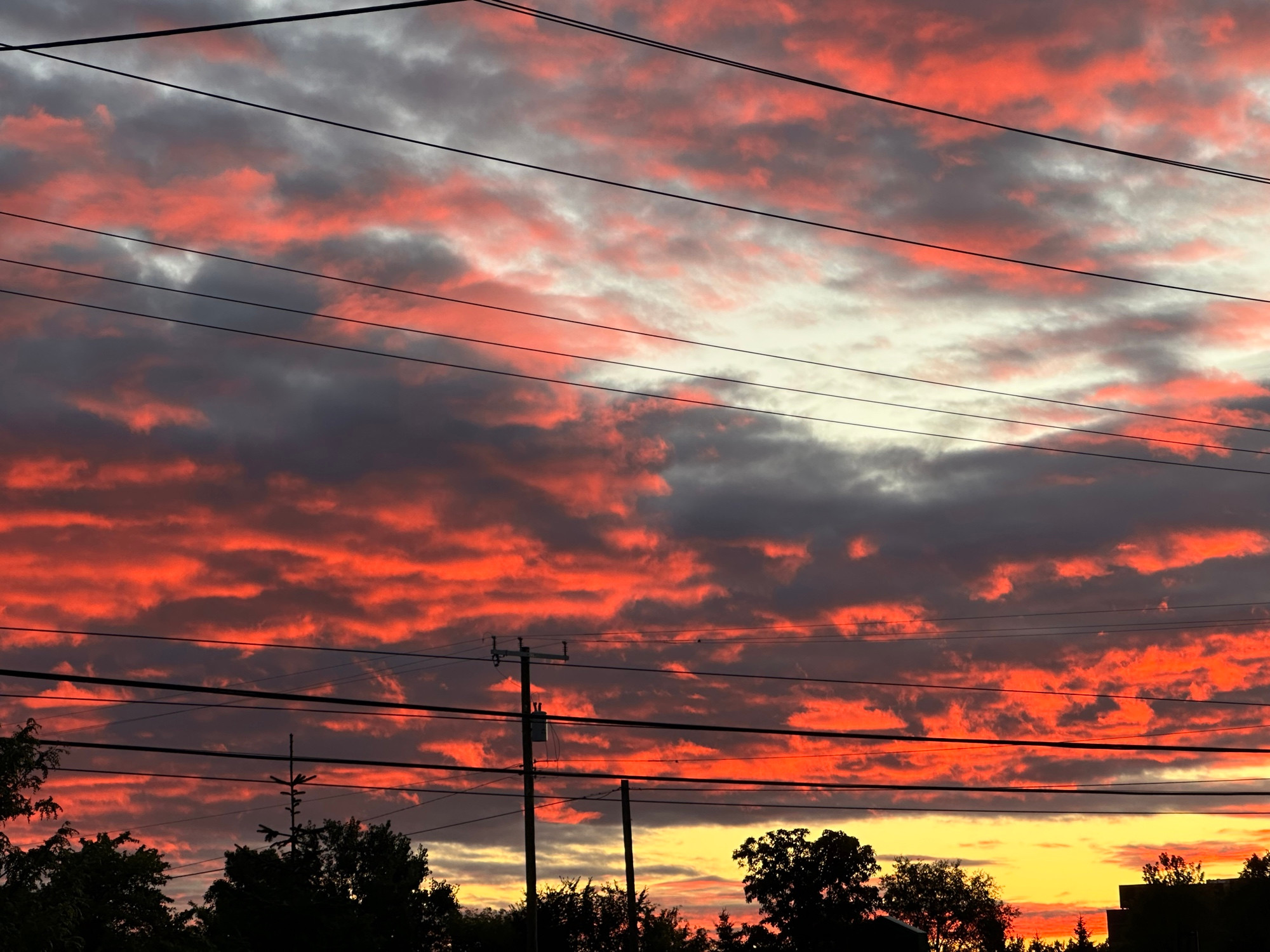 Reddish Orange clouds contrast to dark gray, light blue, and yellow forming a lovely sunrise for you