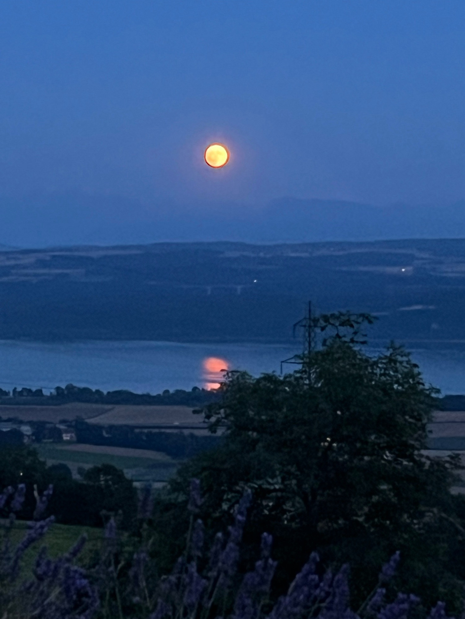 Levé de lune, la lune est orange et se reflète dans le lac.