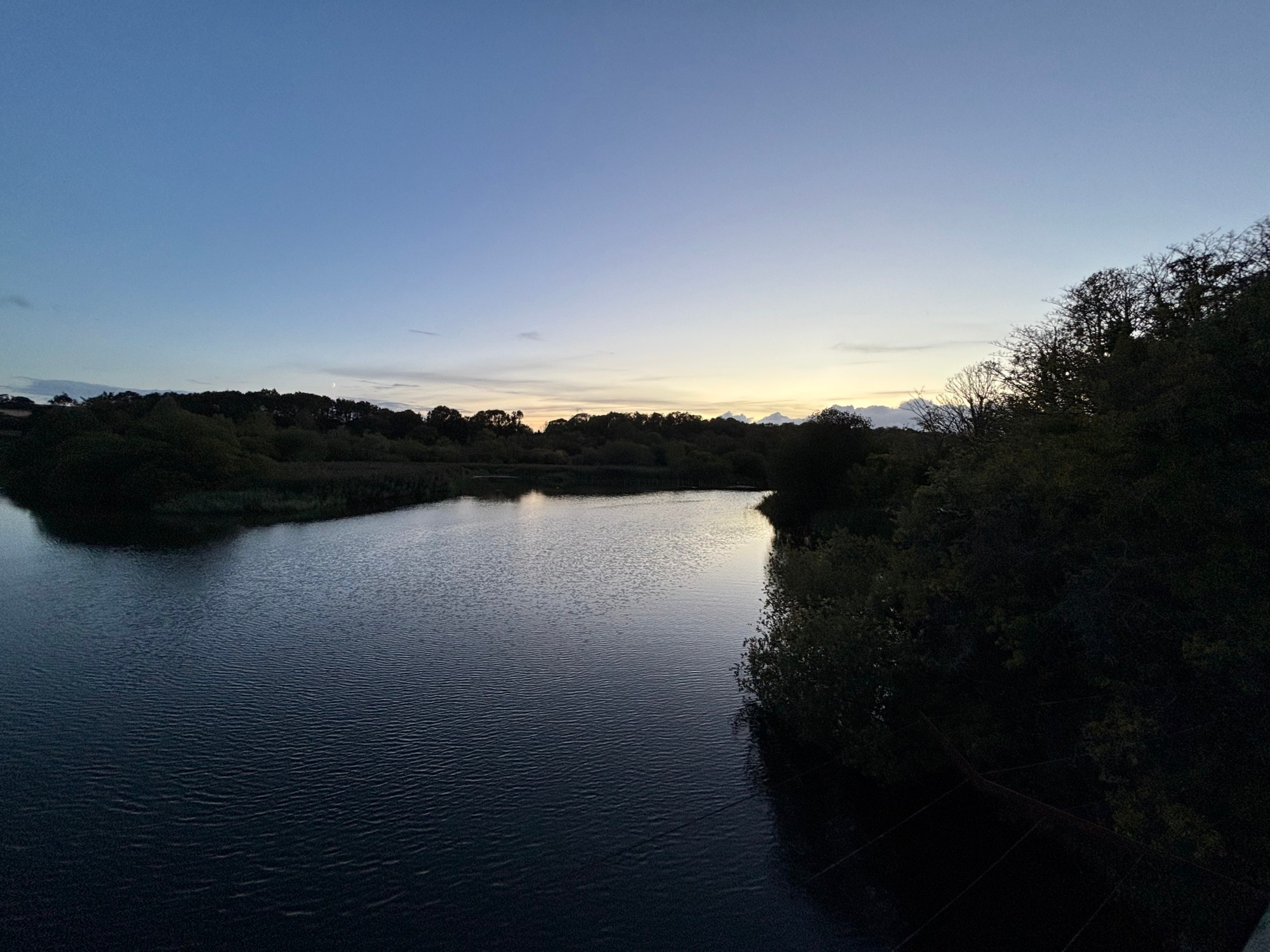 Evening twilight over a small lake. The fading sky is reflected in the water. Trees surround the water’s edge.