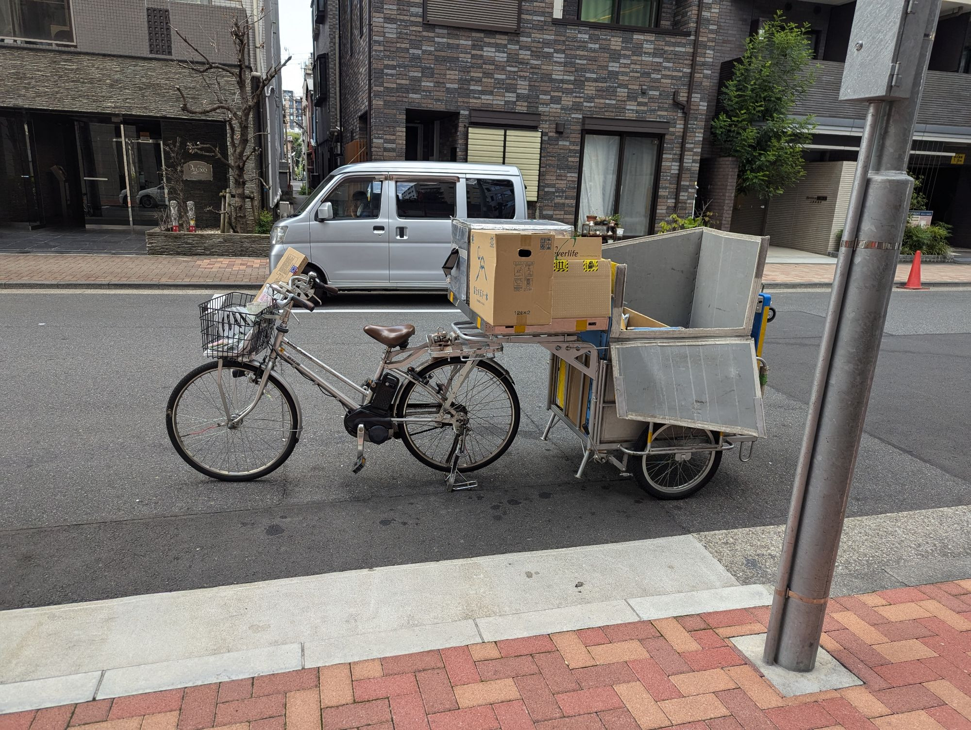 An electric delivery bike with very comfortable step-through upright geometry, a leather seat, large front basket and extremely large cargo trailer on two wheels. Boxes are stacked on the rear rack attaching the trailer.