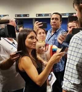 Emmy Award-winning sports Alanna Rizzo in a sharp, shoulderless black dress and (seemingly?) holding a baby in one arm while a microphone in the other as she interviews a baseball player in a crowded locker room. 

She looks so good doing journalism