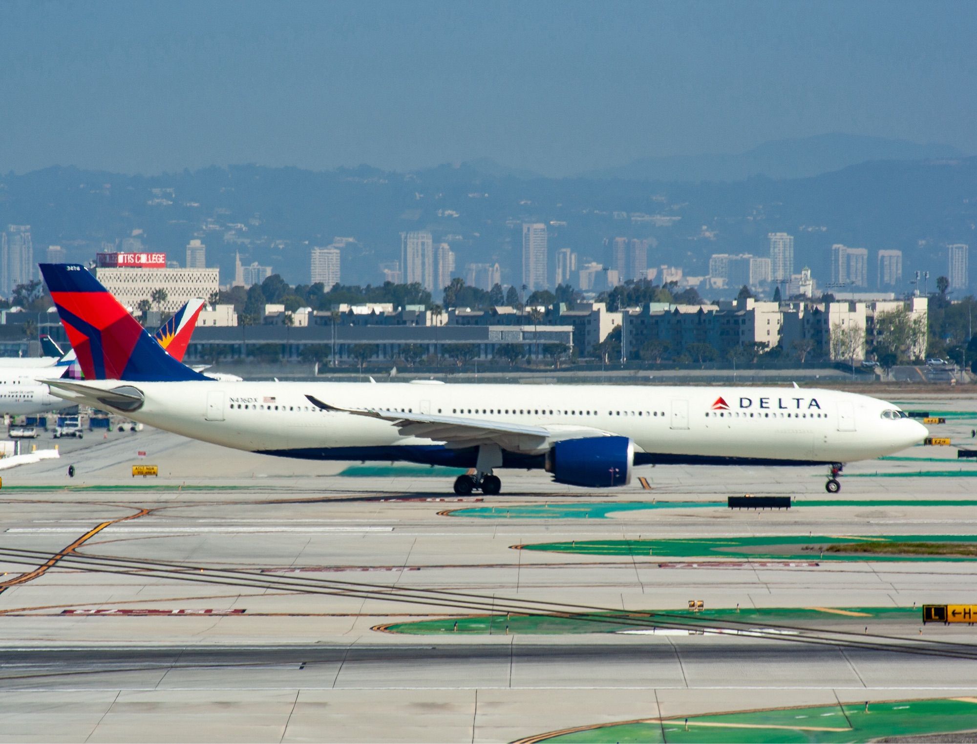 A white jetliner with navy blue tail engines and belly sporting the red Delta logos on the tail and fuselage taxiing to the gate