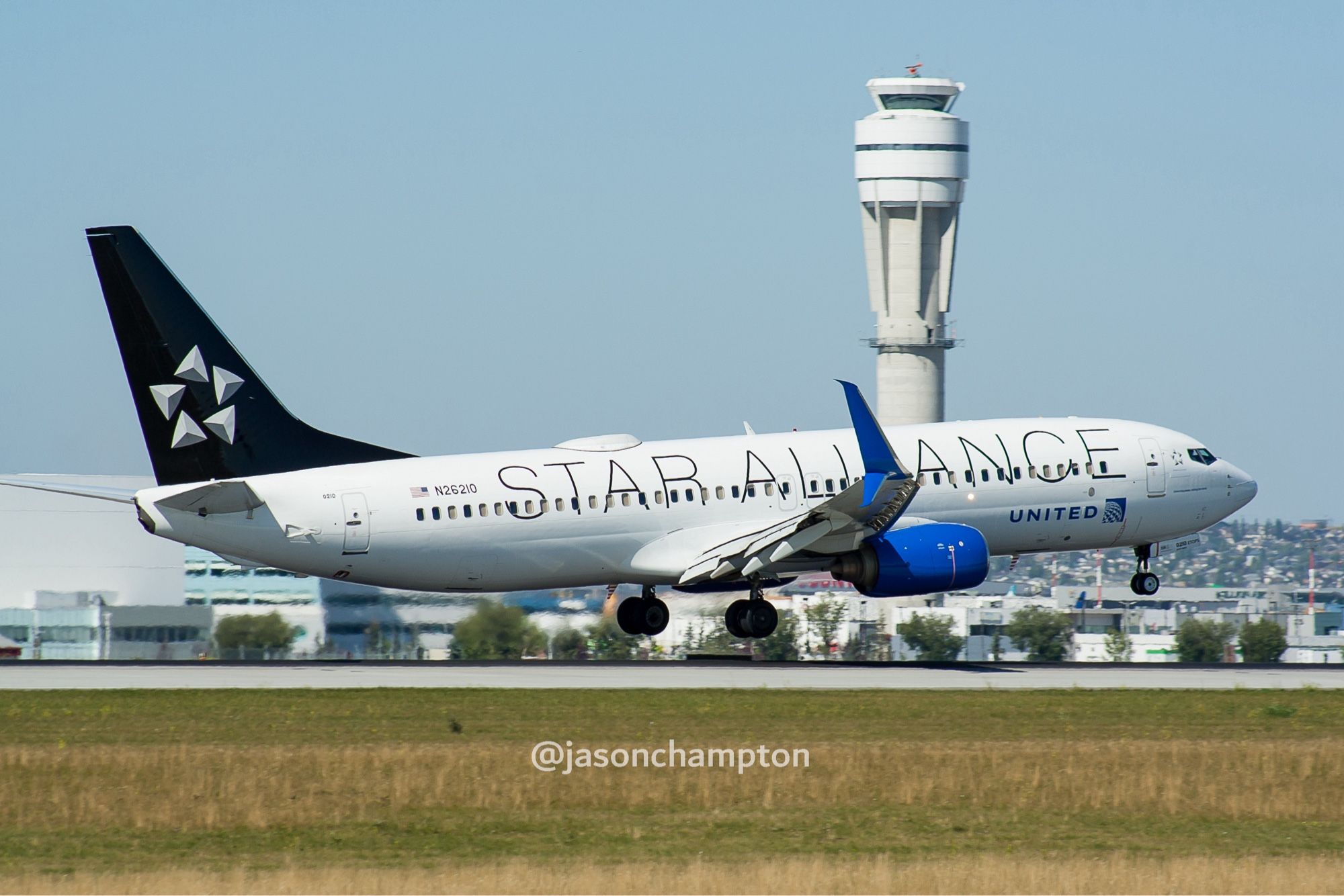 A white jetliner with black tail and blue engines landing. Features the Star Alliance silver star logo and wordmark.