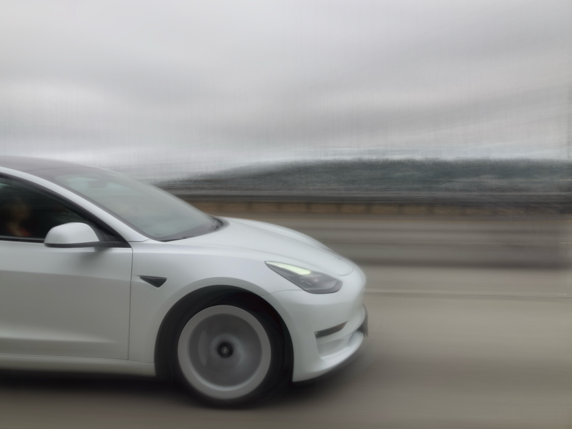 A white Tesla on a highway, the background is blurred