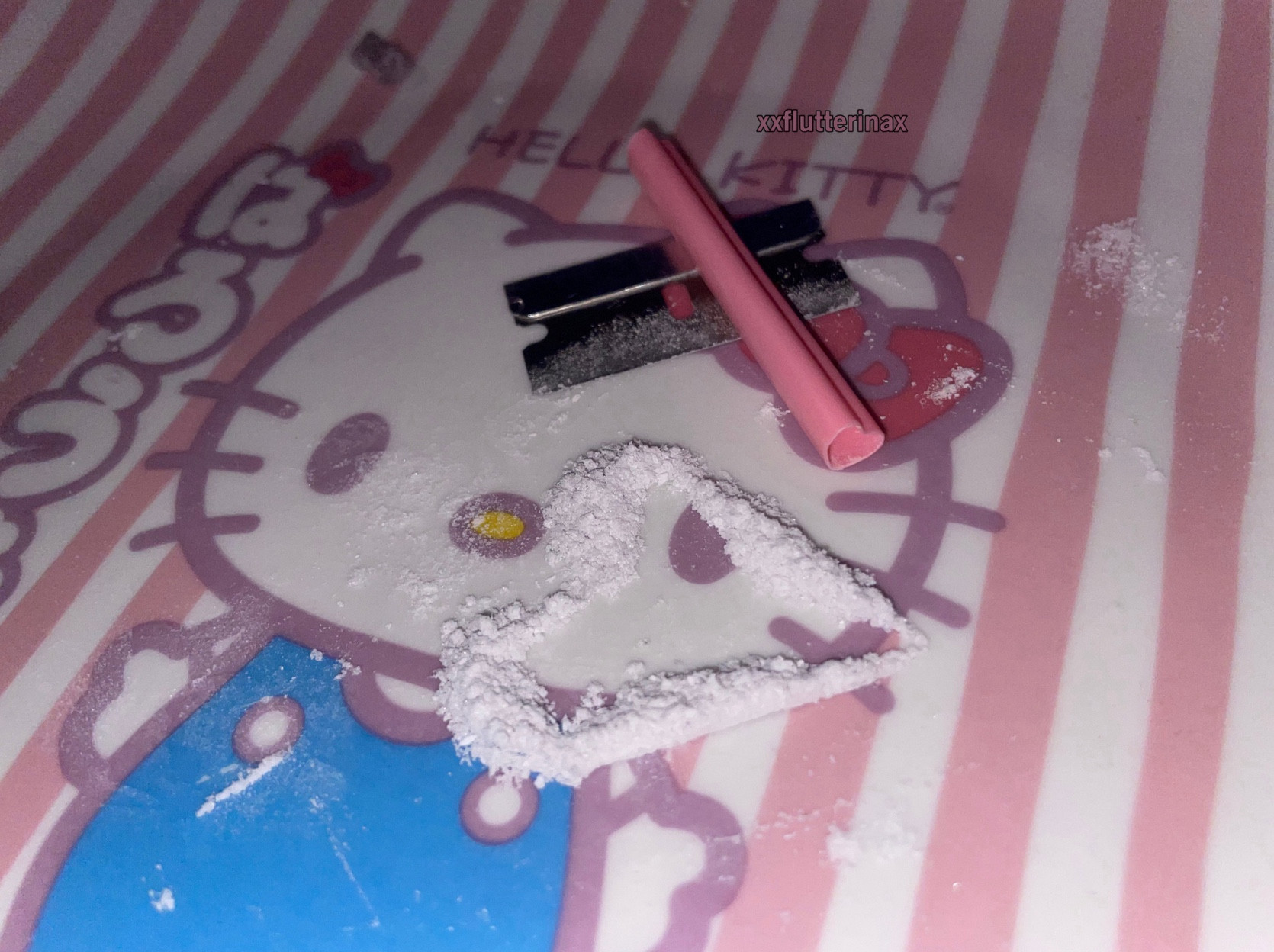 a close up photo of white powder on a pink-and-white-striped, hello kitty plate. the powder is arranged in the shape of an angular heart. there is a short piece of a pink, heart shaped straw resting on top of a single-edged razorblade. there is white powder residue on the end of the straw and along the blade. in the background is a chunk of an unknown, purple, crystalized substance.