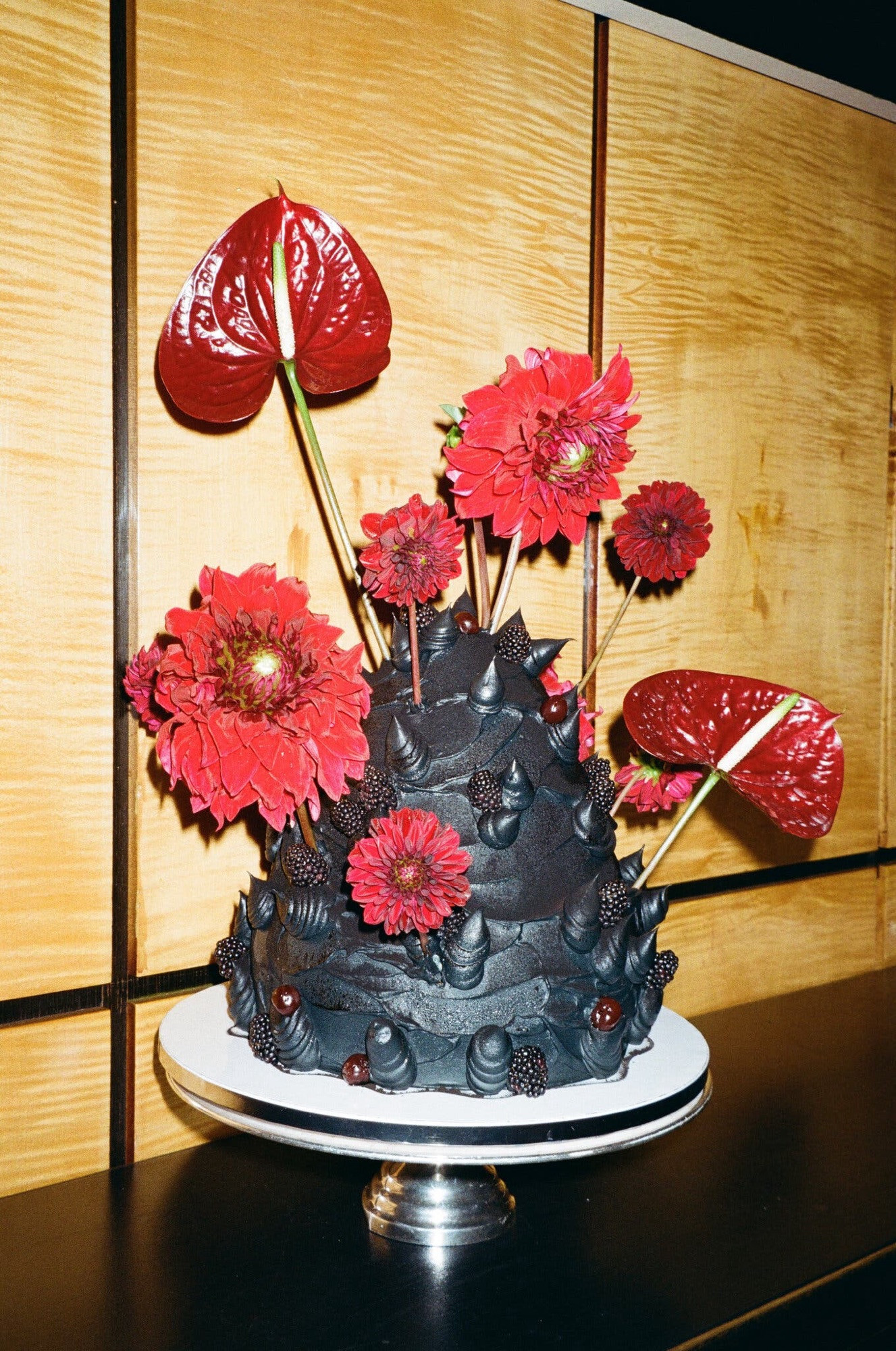 A wedding cake that is a dark brown mound with suggestive branch protuberances, red zinnias and tiger lilies.