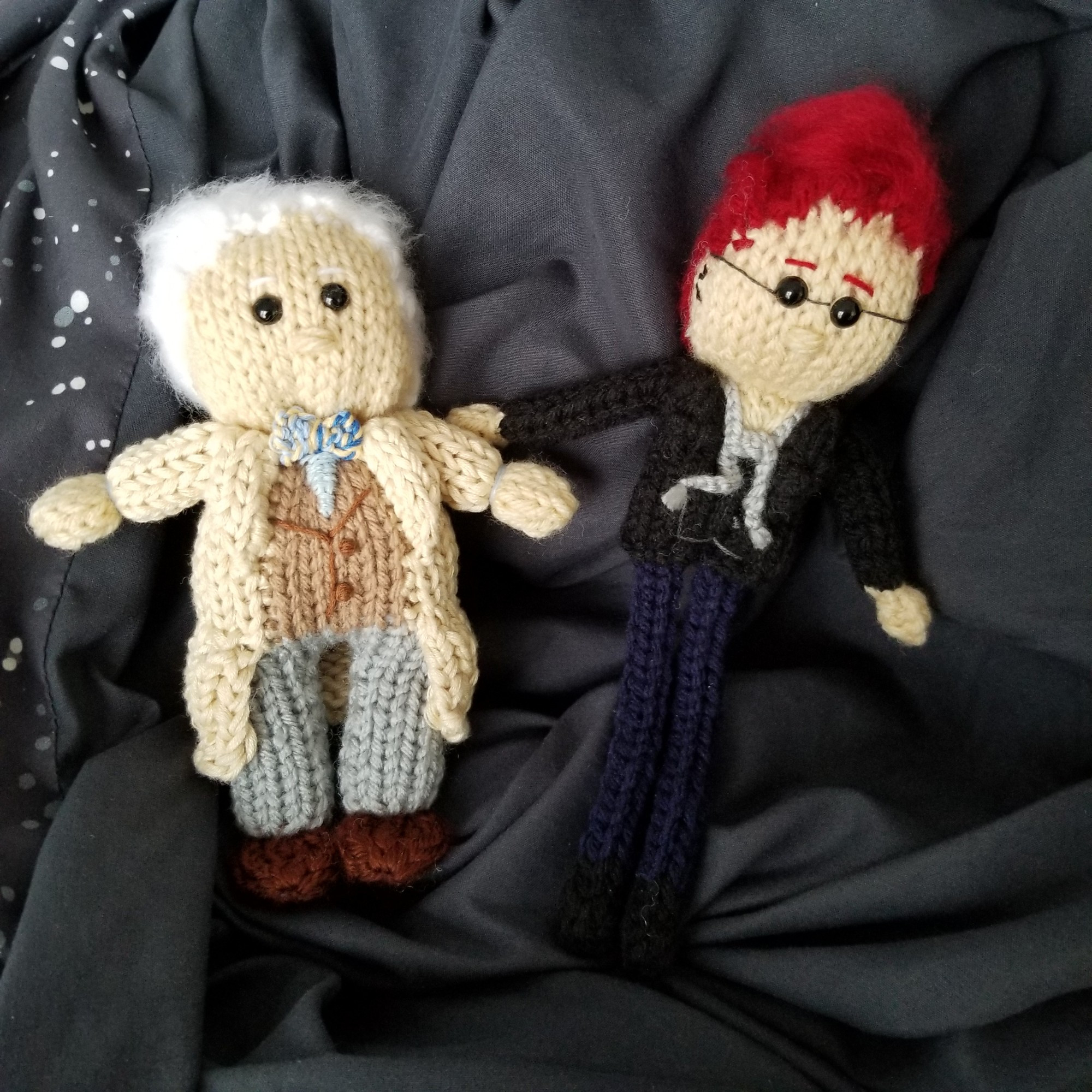 Two knit dolls of Aziraphale and Crowley. Both are wearing their Amazon Prime modern day season one outfits.