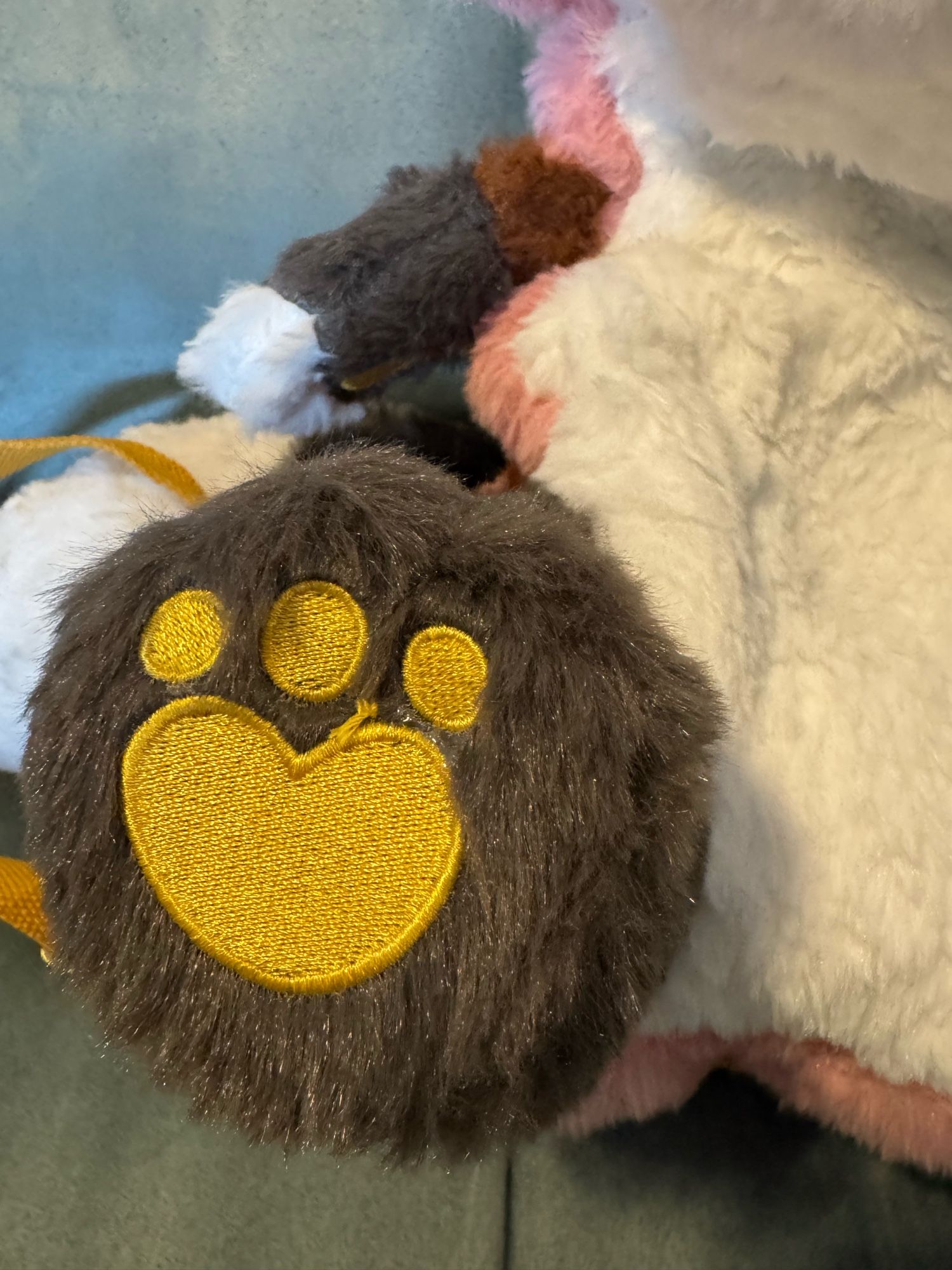 Close-up photo of the plush’s brown furry paw showing a tiny bit of embroidery topper/stabilizer and a knotted thread next to the cute heart-shaped embroidered yellow paw pads.