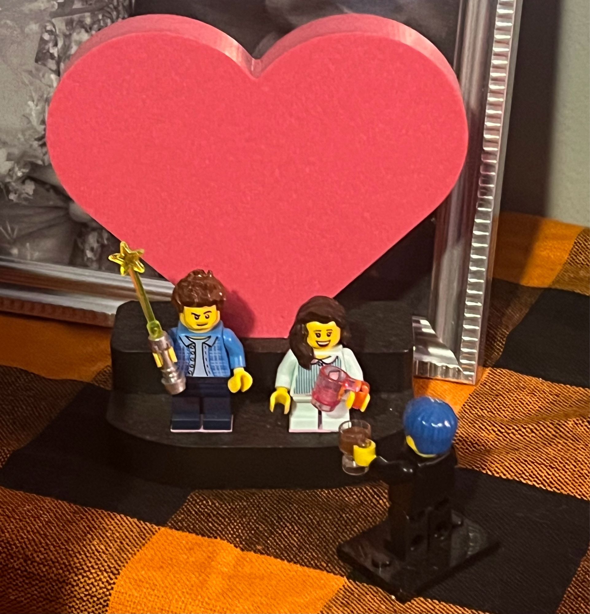 Lego minifigures of Ryan and Courtney being married by a Lego minifigure of me. They’re on a stand with a big heart behind it.