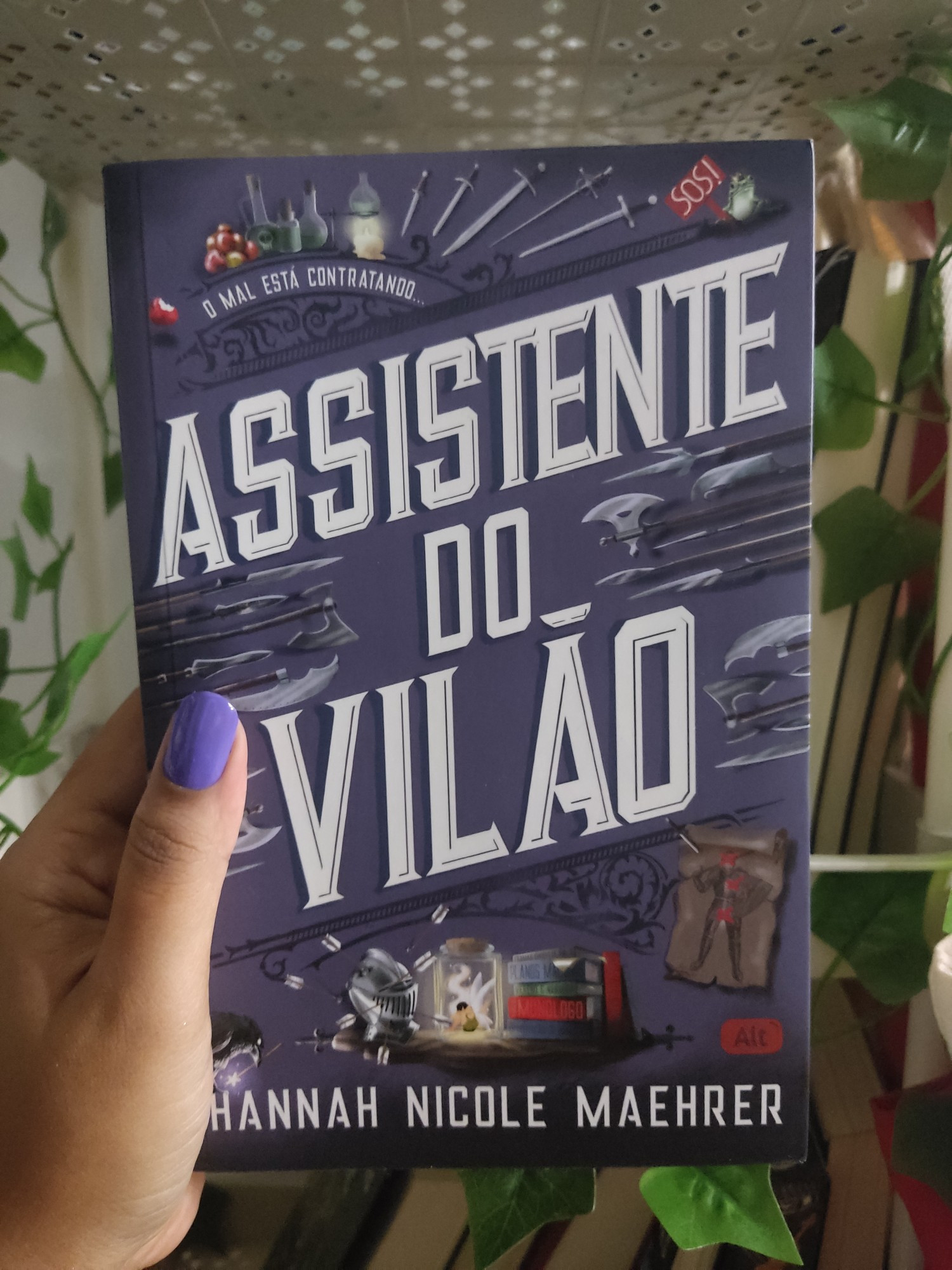 Foto da capa do livro assistente do vilão de Hannah Nicole Maehrer. A capa é roxa, o título no centro, ocupa a maior parte do livro, nas laterais e na parte superior há armas como punhais, espadas e foices de tamanhos e formas variadas, no parte de baixo há um elmo cheio de flechas, uma fada presa em um pote e livros, no topo também há venenos, maçãs e um sapo usando coroa segurando uma plaquinha escrita SOS.