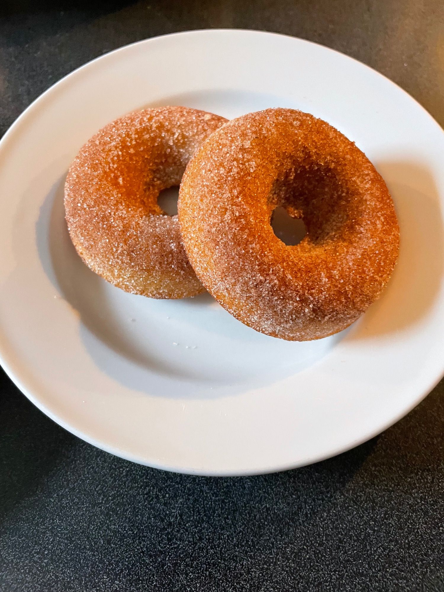 Two cinnamon sugar coated apple cider doughnuts sitting on a white plate.