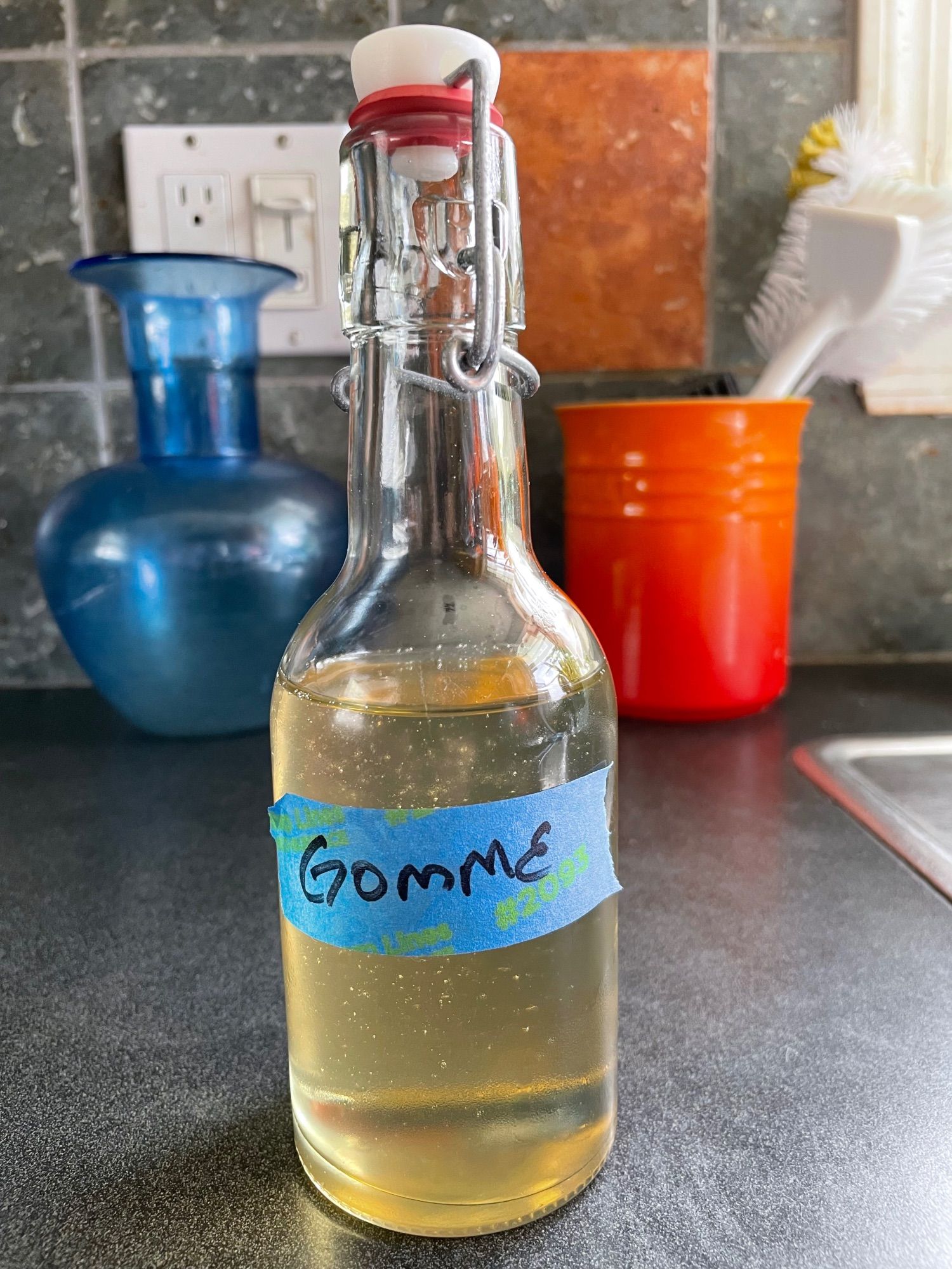 A capped bottle of a clear-ish tan liquid labeled "gomme". Gomme syrup is a 2:1 sugar/water syrup made with food grade gum arabic as a thickener used in cocktails in place of simple syrup to provide a "silkier" drink.