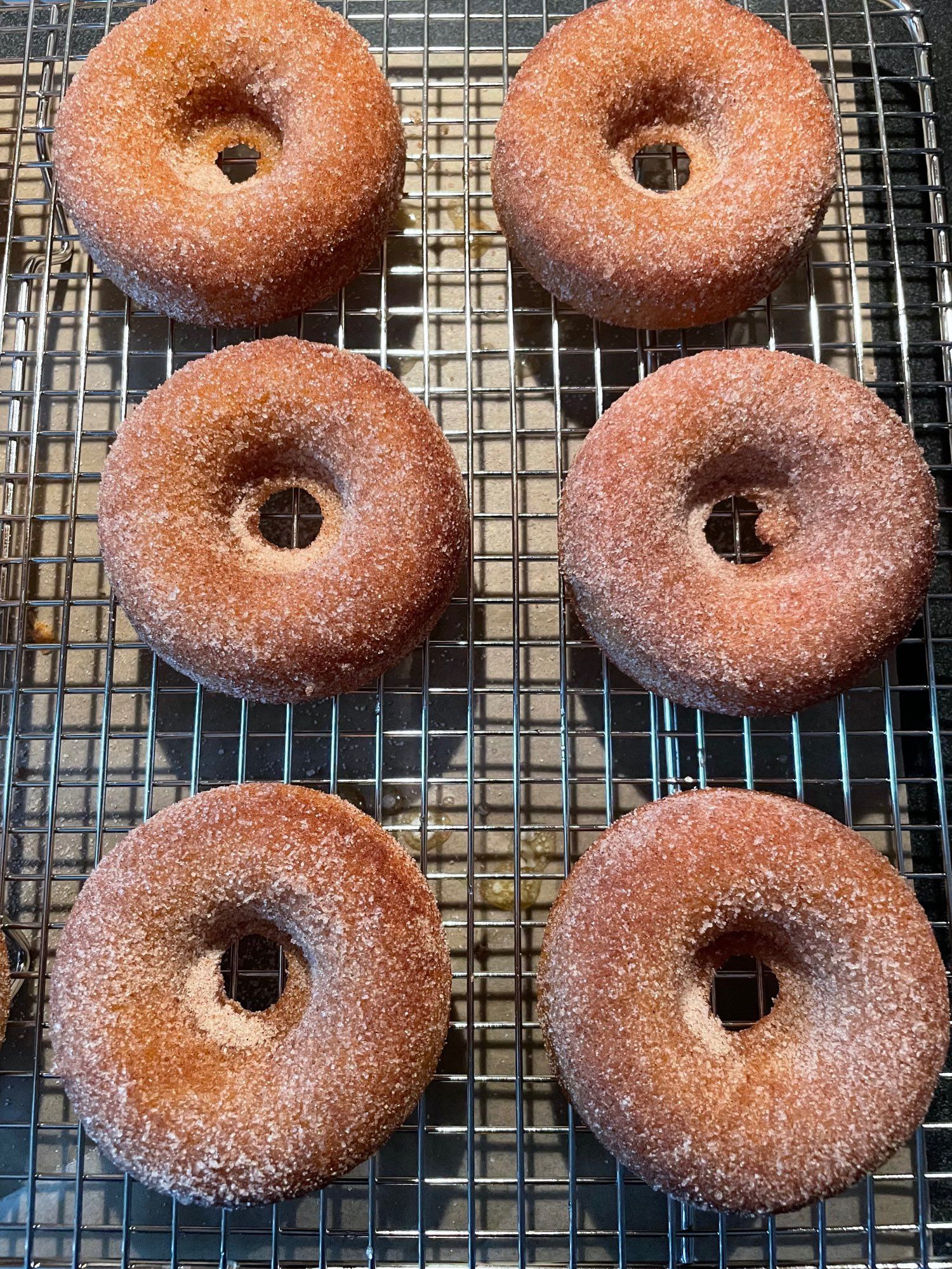 Six cinnamon sugar coated apple cider doughnuts on a wire rack.