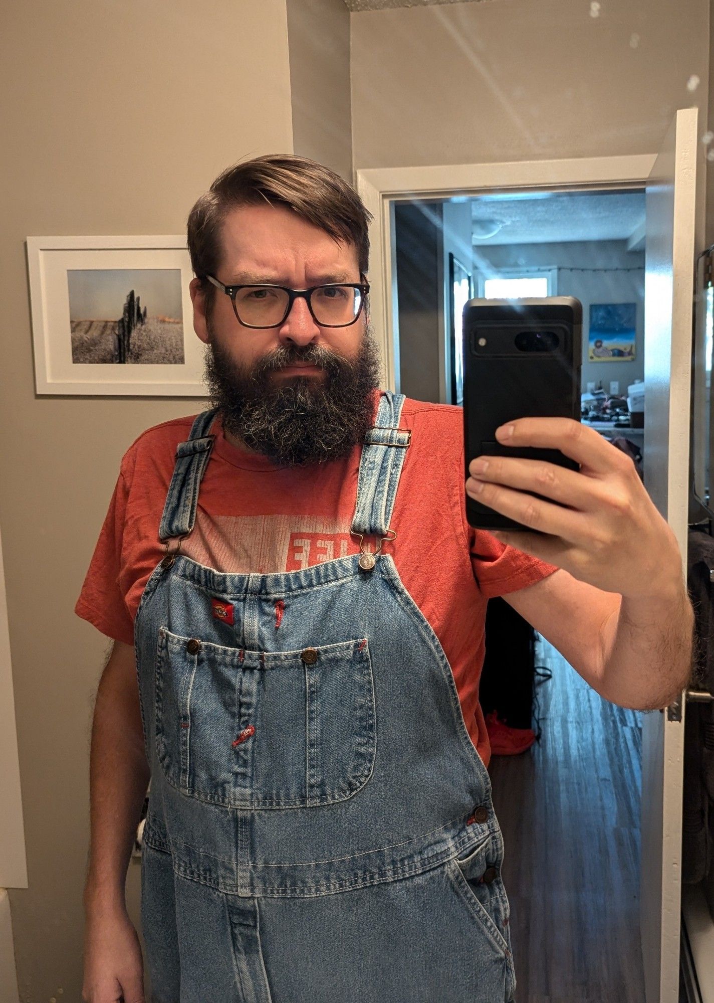 The same bearded man in a pink T-shirt and denim overalls.