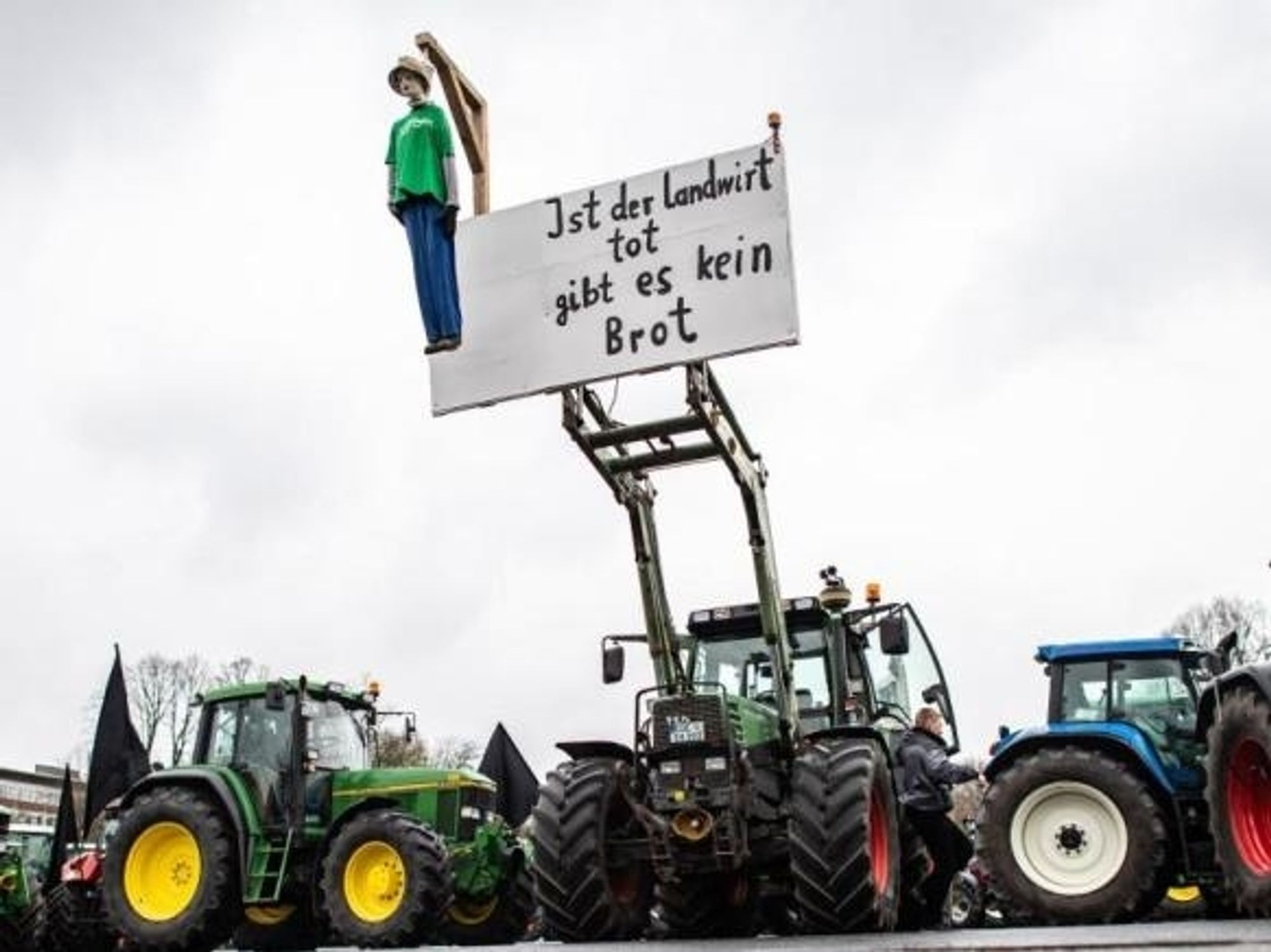 Drei Traktoren. An mittleren Traktor hängt ein Galgen mit einer grün angezogenen Puppe. Daneben ein Schriftzug: Ist der Landwirt tot gibt es kein Brot