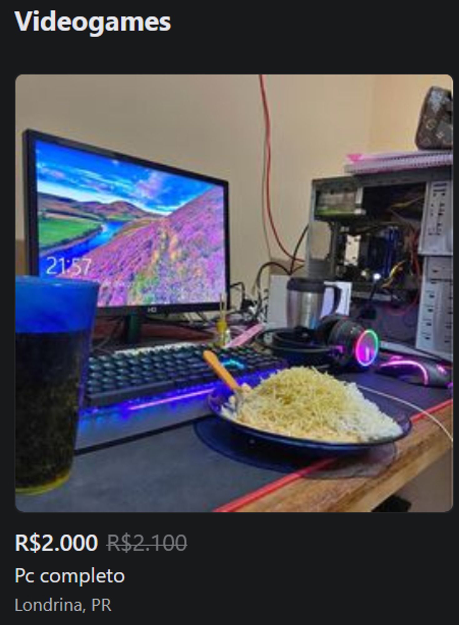 Anúncio de um PC Gamer no facebook.
A imagem apresenta uma mesa com um gabinete de PC aberto, um headphone RGB, um monitor, um teclado, um copo de refri e um prato de comida tipo de estivador cheio de arroz e batata palha.
Preço: R$ 2.000