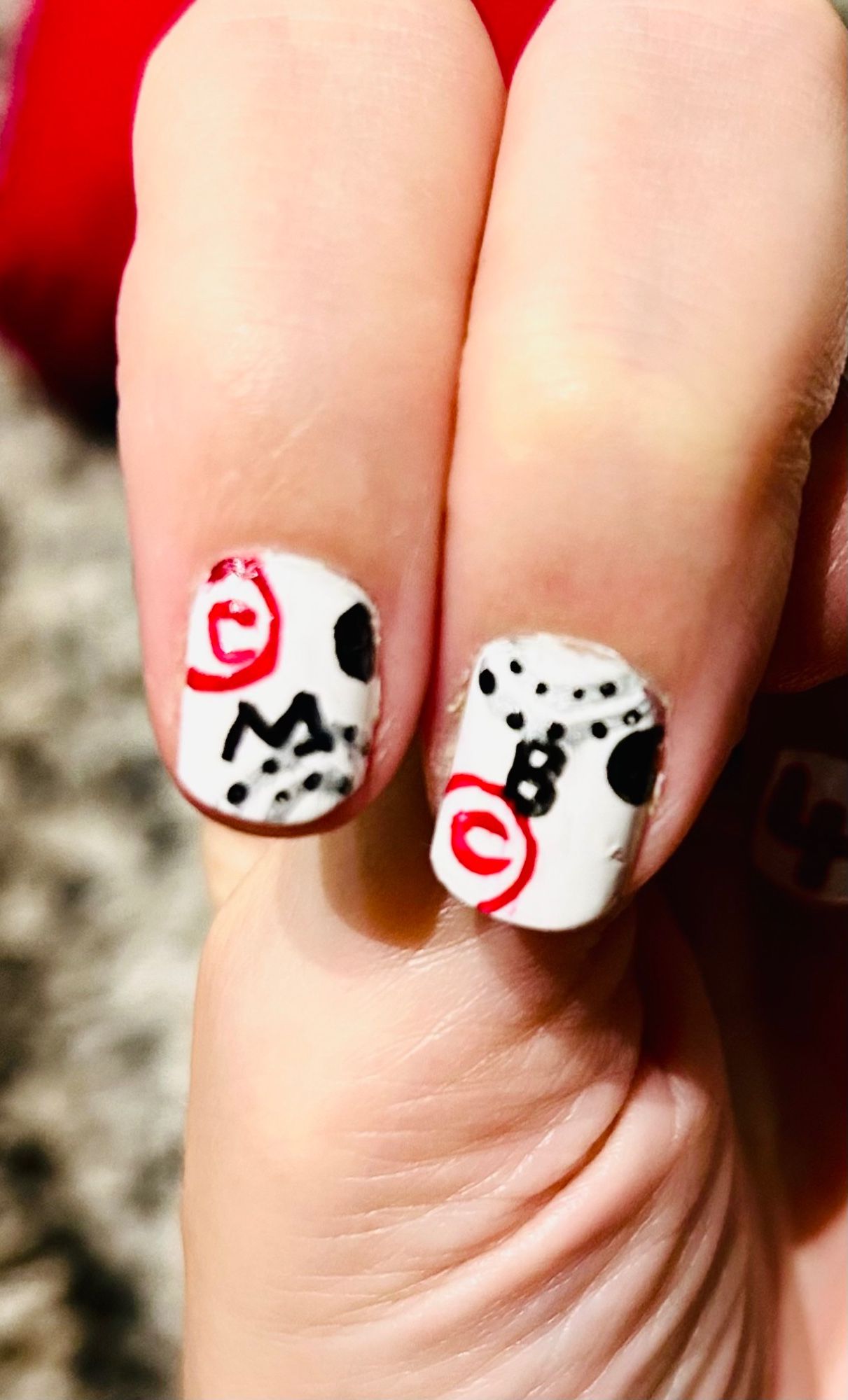 Two nails with the letters M and B on them—nails are white with silver and black detailing and red “copyright” symbols