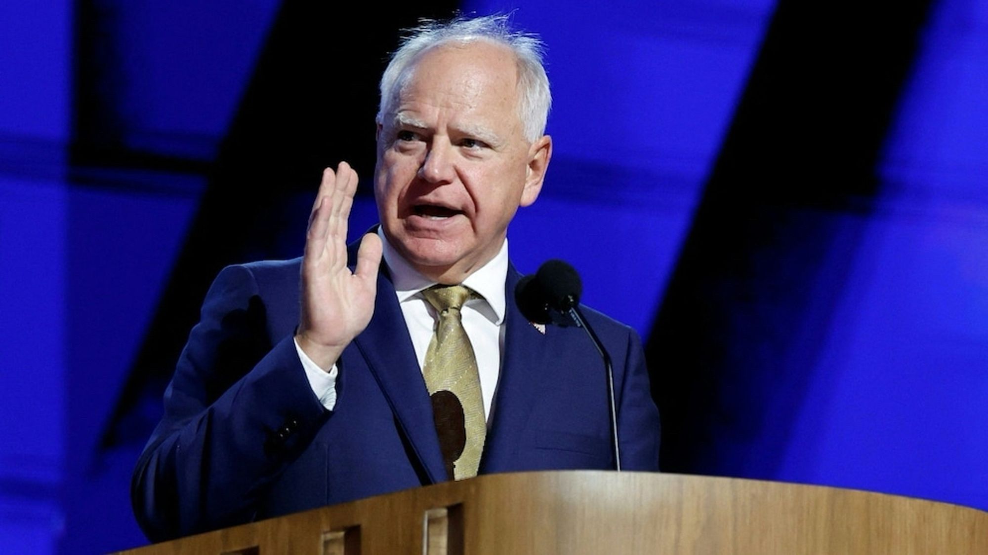 Walz in suit and tie speaking with open hand closer to his mouth