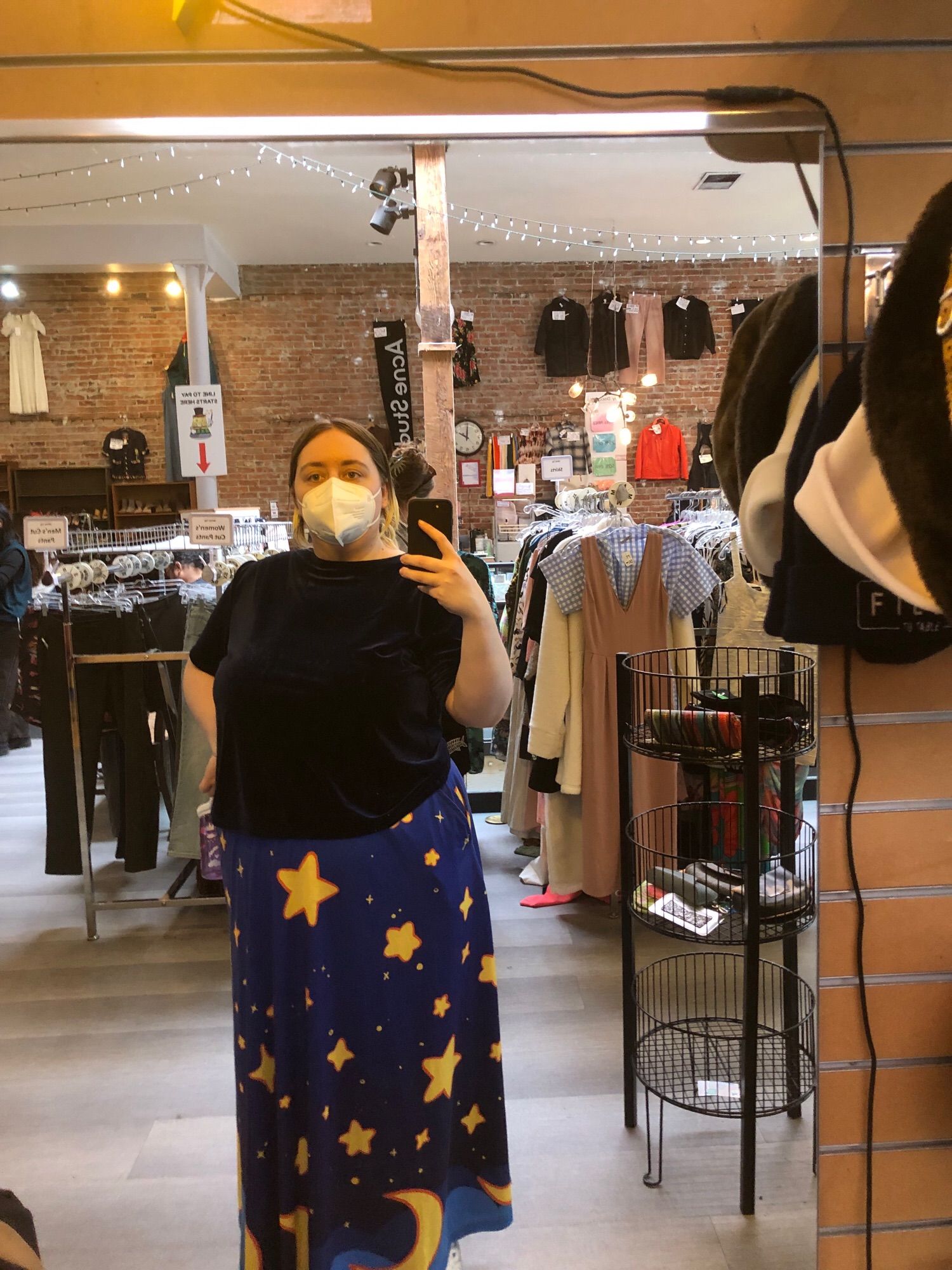 Sara taking a mirror selfie: she has a blue shirt, a star patterened floor length skirt, and her hair in a ponytail.