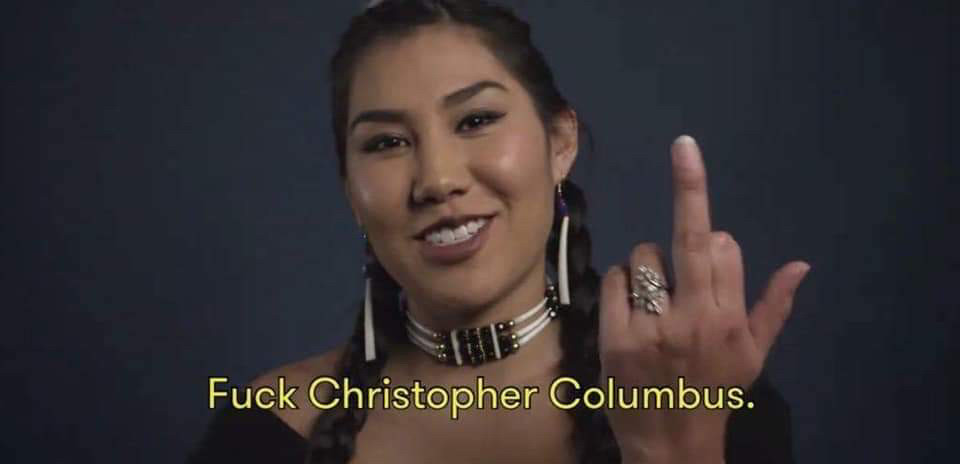 Image of an indigenous woman flipping the bird and smiling. The caption reads: Fuck Christopher Columbus.