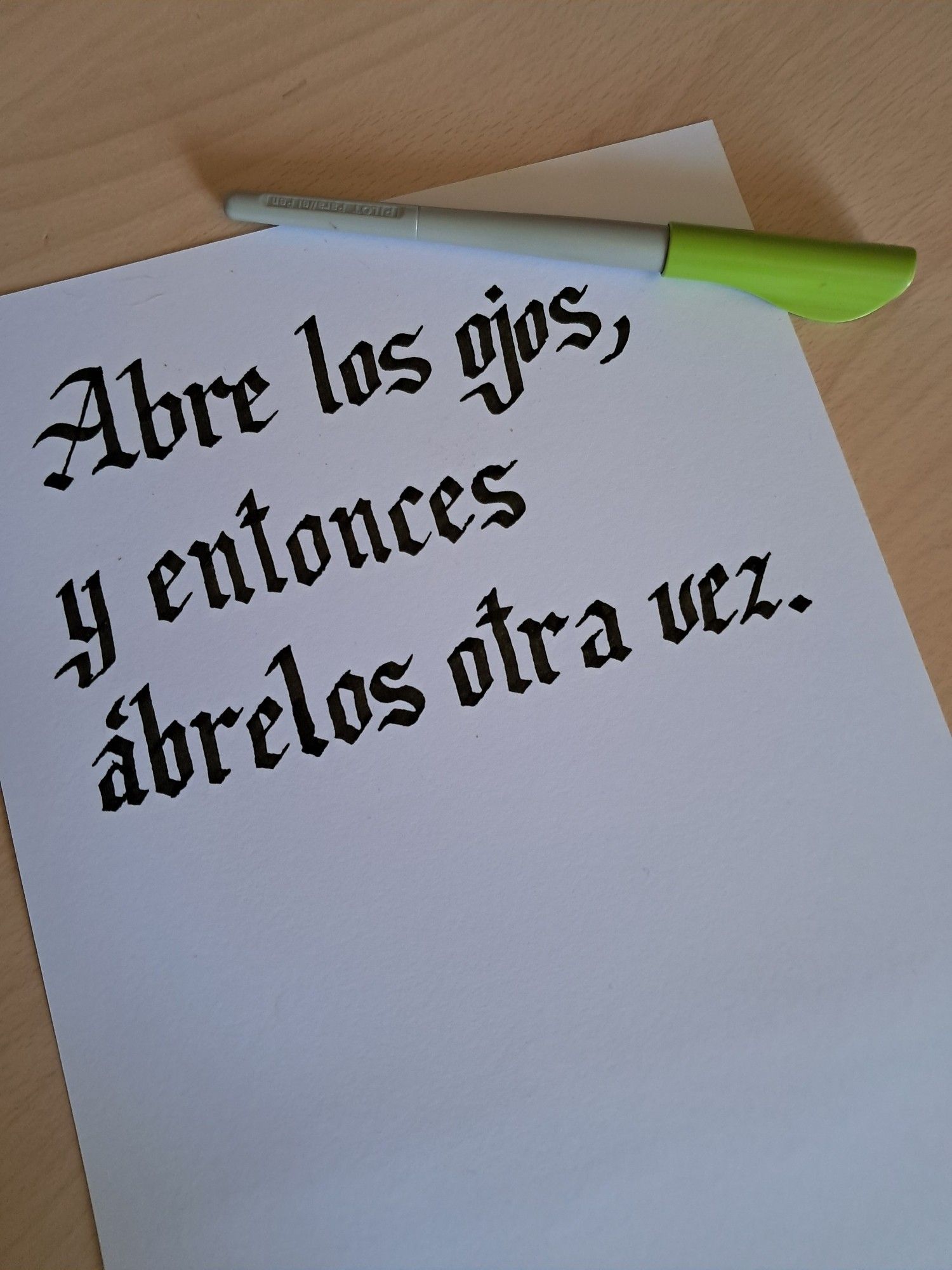 La frase "Abre los ojos, y entonces ábrelos otra vez" escrita en caligrafía gótica con tinta negra. Encima, el Pilot Parallel Pen empleado.