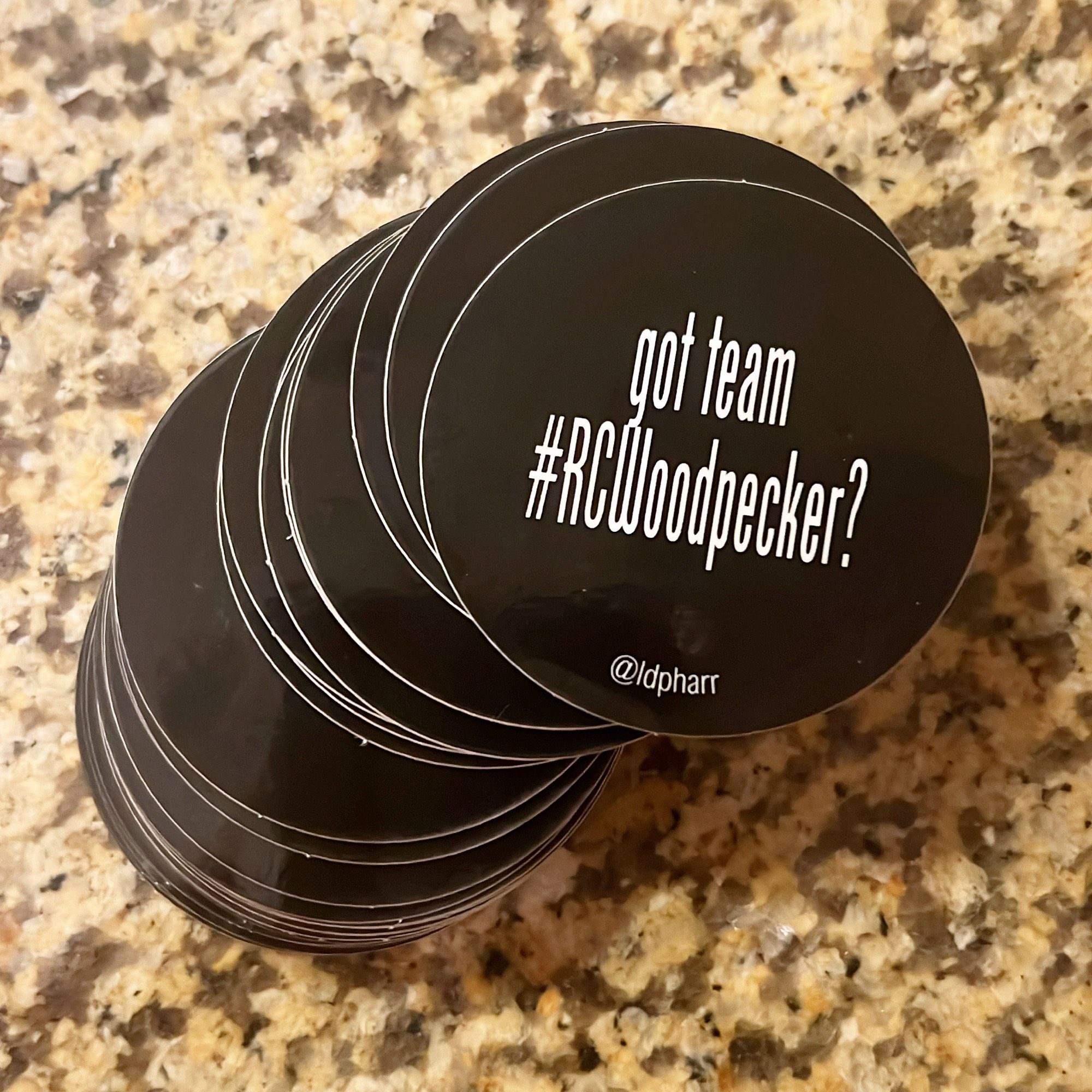 A stack of black circle stickers that read got team #RCWoodpecker? @ldpharr