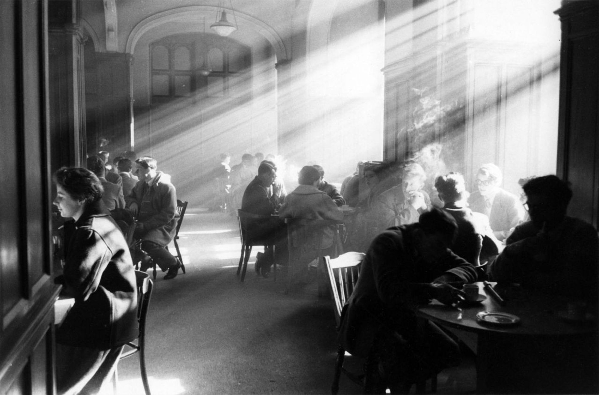 photo
an interior
light streams in from the windows to the right, the thick cigarette smoke showing the light in beams
people sit around tables arguing the finer points of obscure knowledge