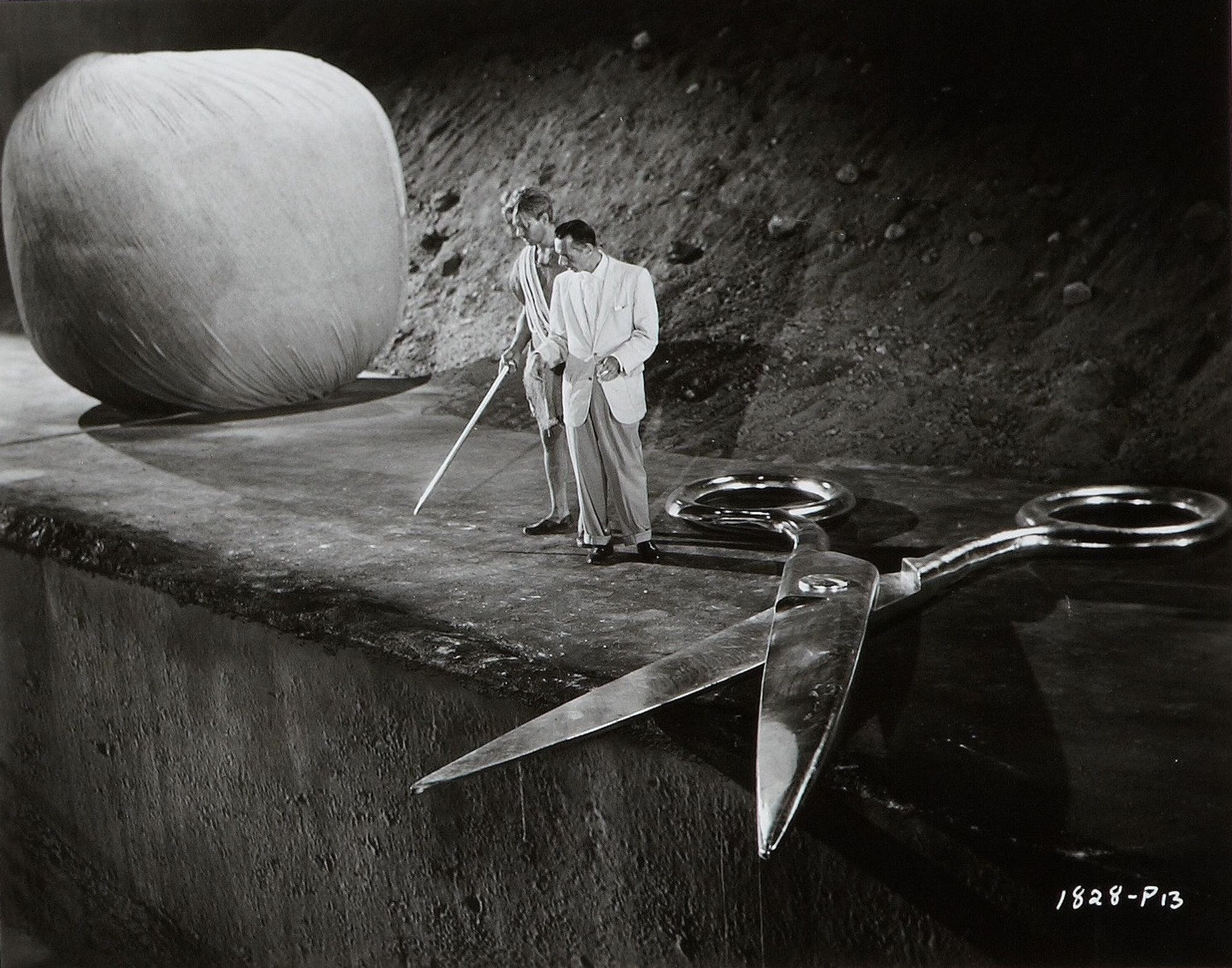 two people next to a giant pair of scissors and a huge ball of yarn.