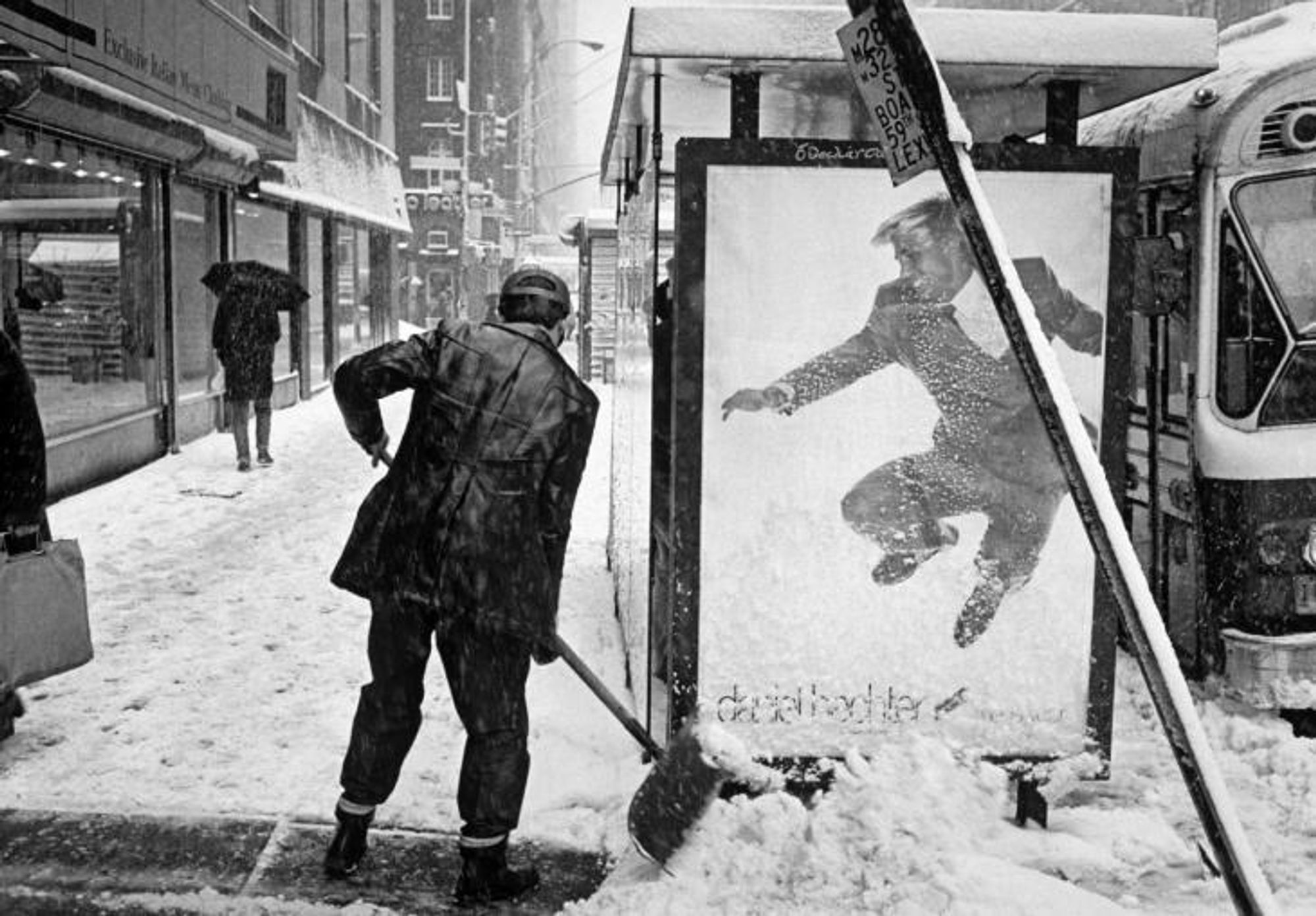 photo
a man shoveling snow next to a bus shelter. A poster on the bus shelter is a man leaping in the air. It looks like the poster man is avoiding the shovelled snow.