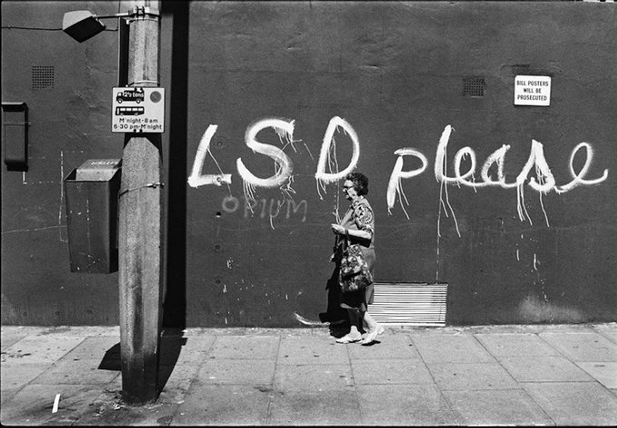 photo a person walking past a wall. on the wall is sprayed LSD please