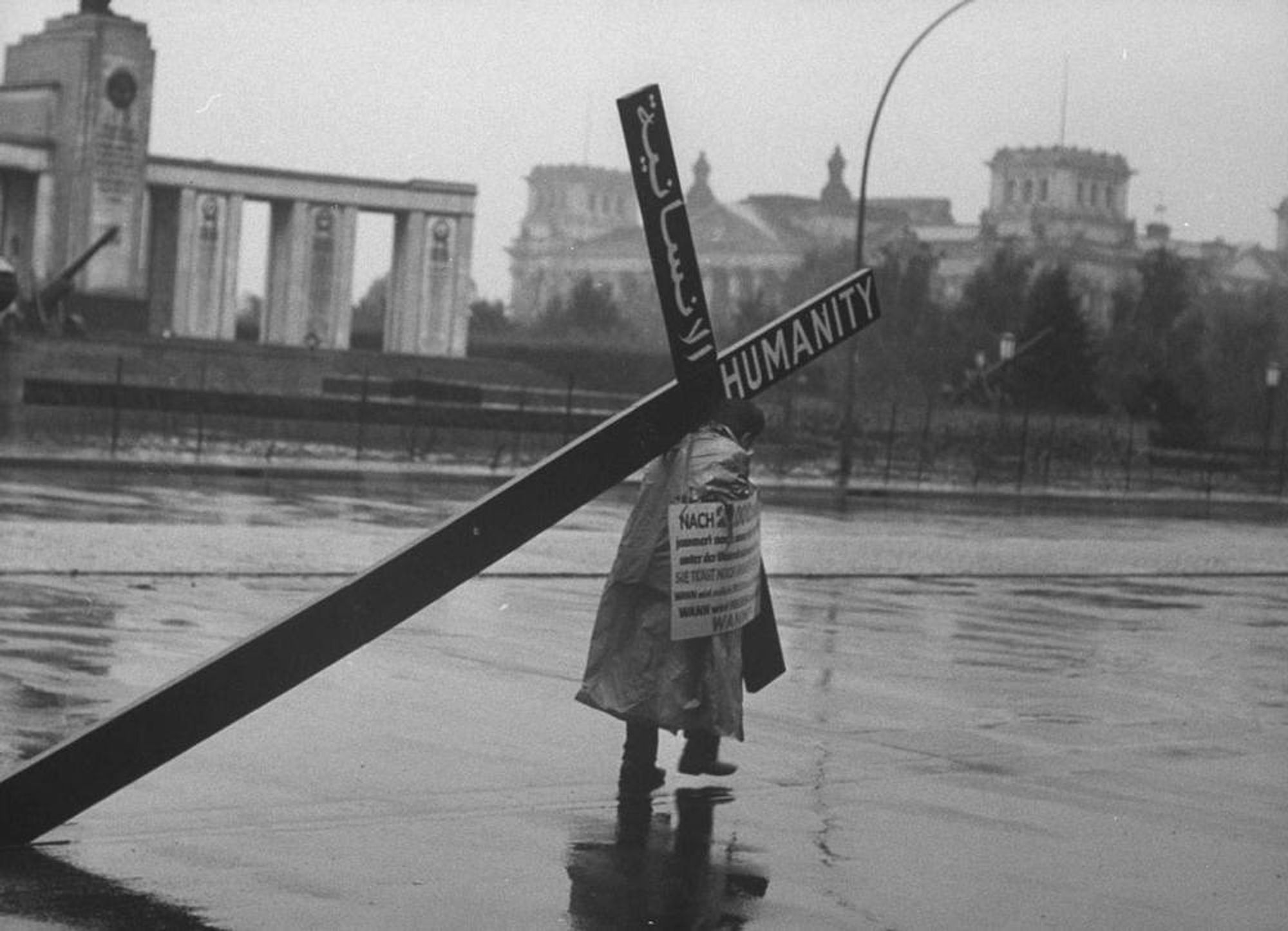 photo
a man carrying a large cross, and wearing a sign. In the background a rain swept city looks on indifferently.