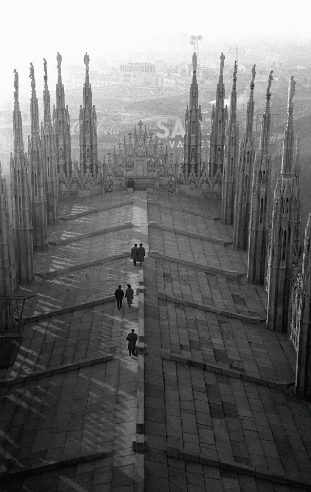 photo
a roof, slighly arched and some people walking on it, a city obscured by mist is below and in the distance. Statues are stood on some ornate pointy bits, (its a technical term, I wouldn't expect you to understand)