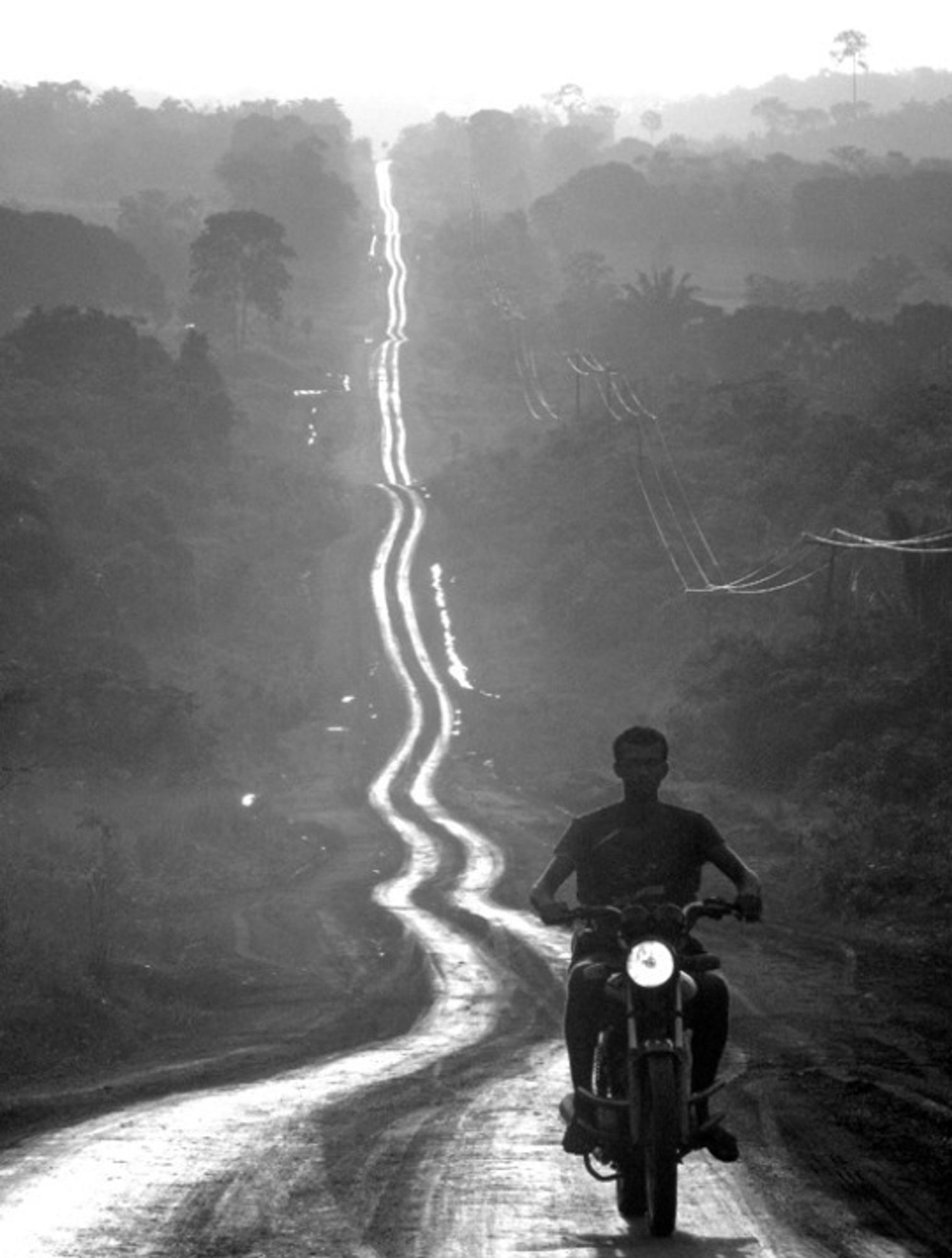 photo
a man on a motorcycle.
the road stretches out behind him like  a shining ribbon, swathing through the landscape.