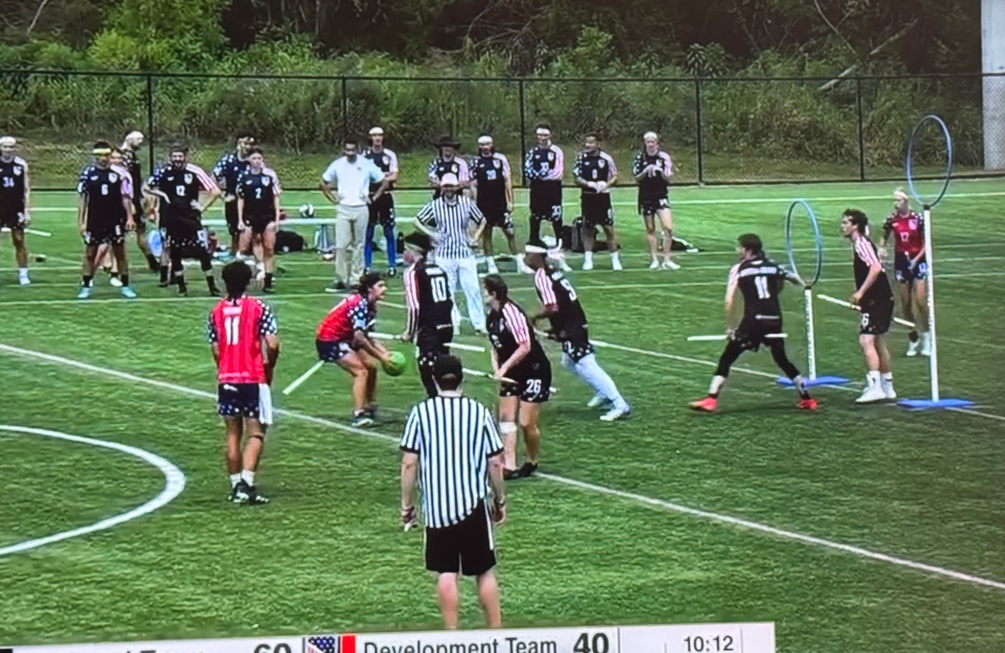 Players on a field with broomsticks between their legs. 