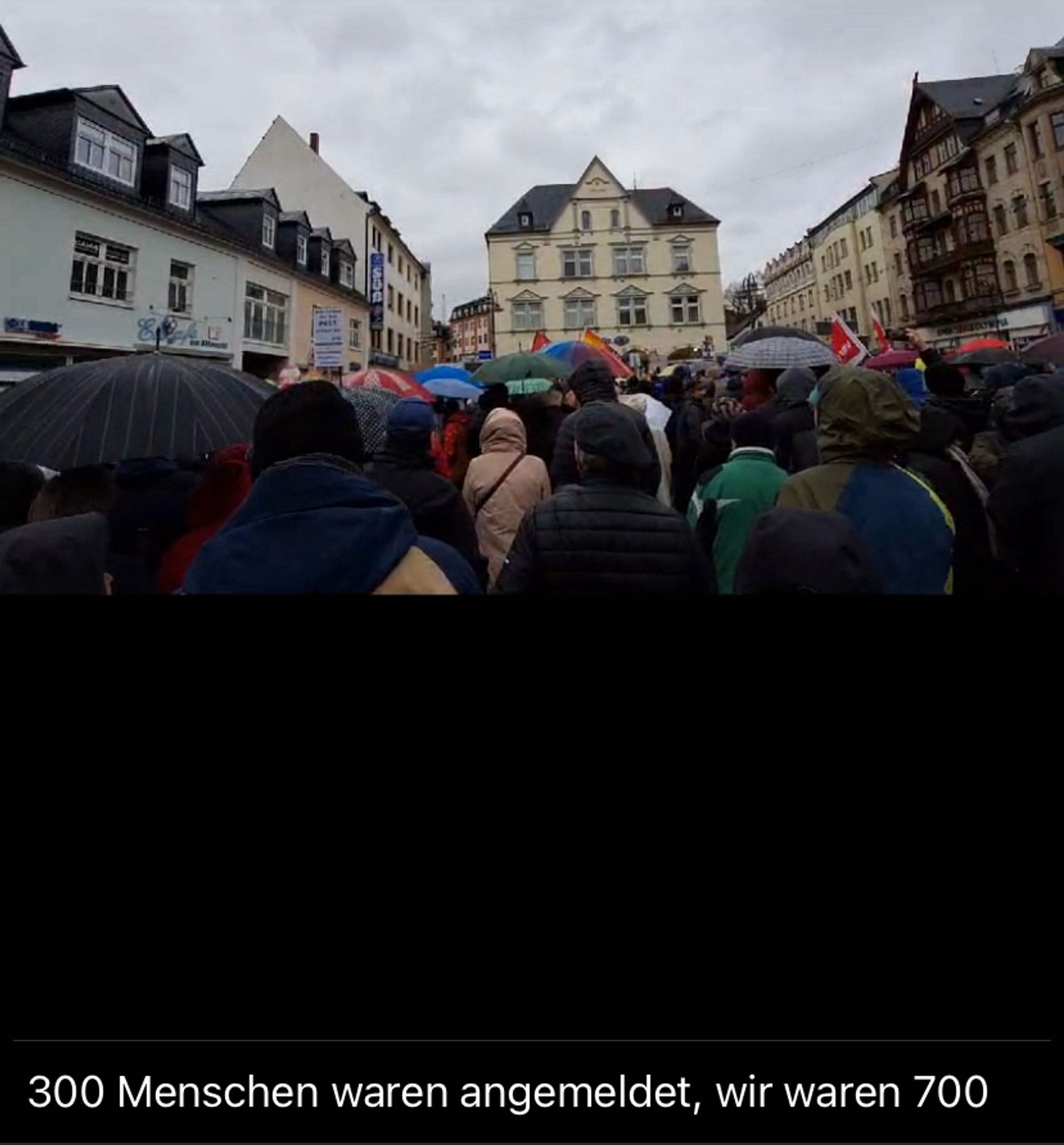 Auf einem Marktplatz steht im Regen eine größere Menschenmasse.