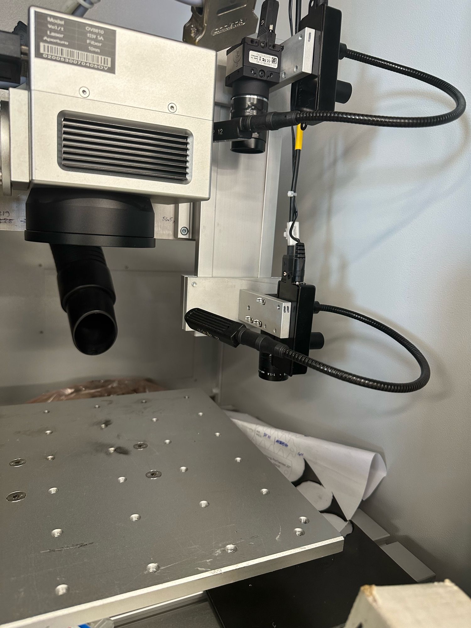 Two cameras are held on a movable axis next to the scanning head of a laser. There is a table with screw holes in a grid pattern underneath the laser head.