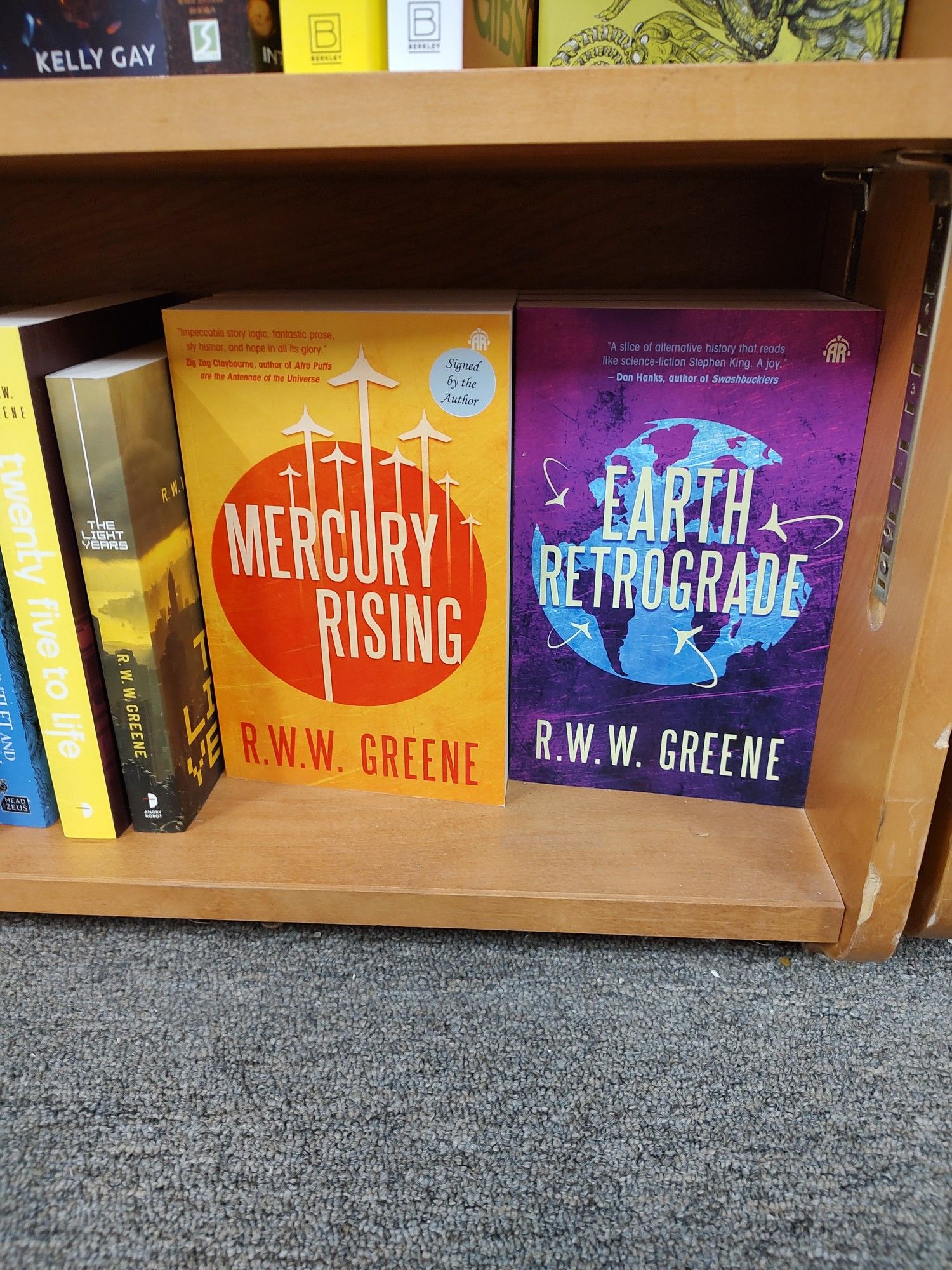 A bookstore shelf that contains "Twenty-Five to Life," "The Light Years," "Mercury Rising," and "Earth Retrograde," all sci-fi novels by R.W.W. Greene