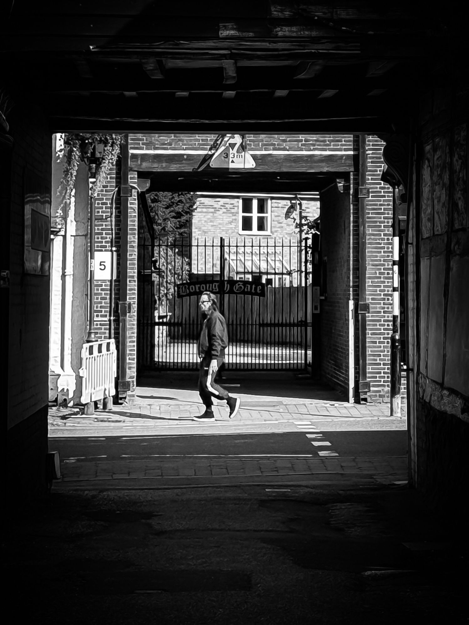 A black-and-white photo of a gateway on a street with a man walking past