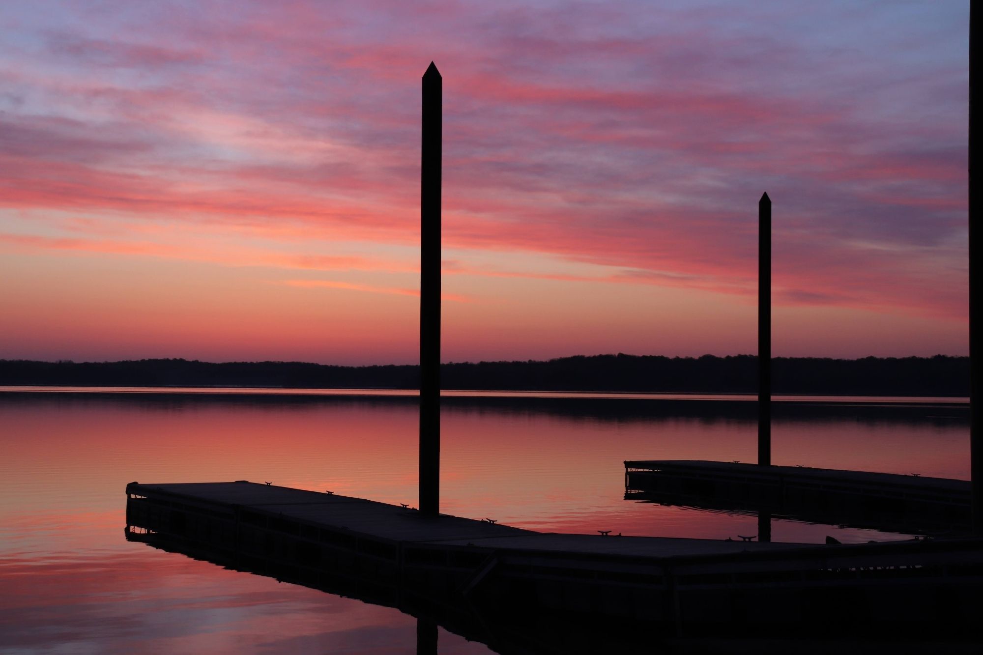 A beautiful pink sunrise lavishes itself on the still surface of a calm, tree-ringed lake. Two piers stretch put onto the water. Everything is serene.